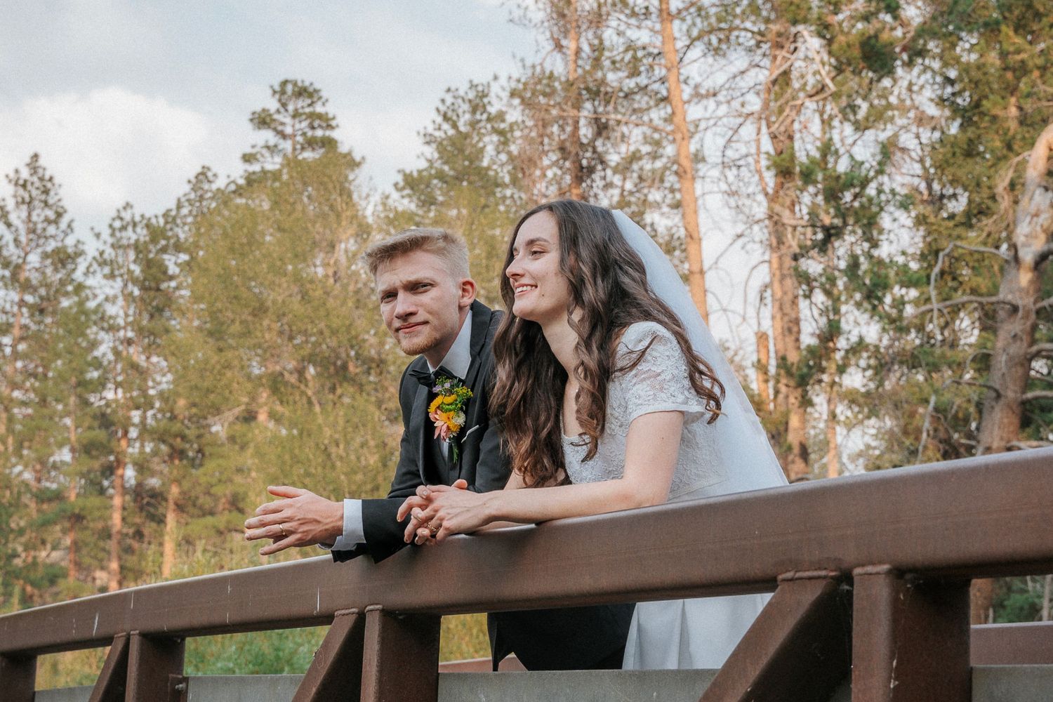 Newlyweds sharing casual moment on wooden deck with forest view.