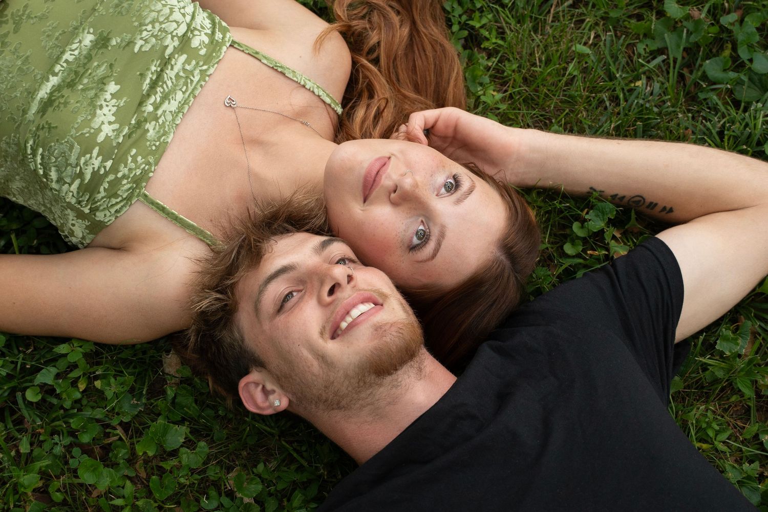 Several people lie in the grass looking up at the sky with relaxed expressions.