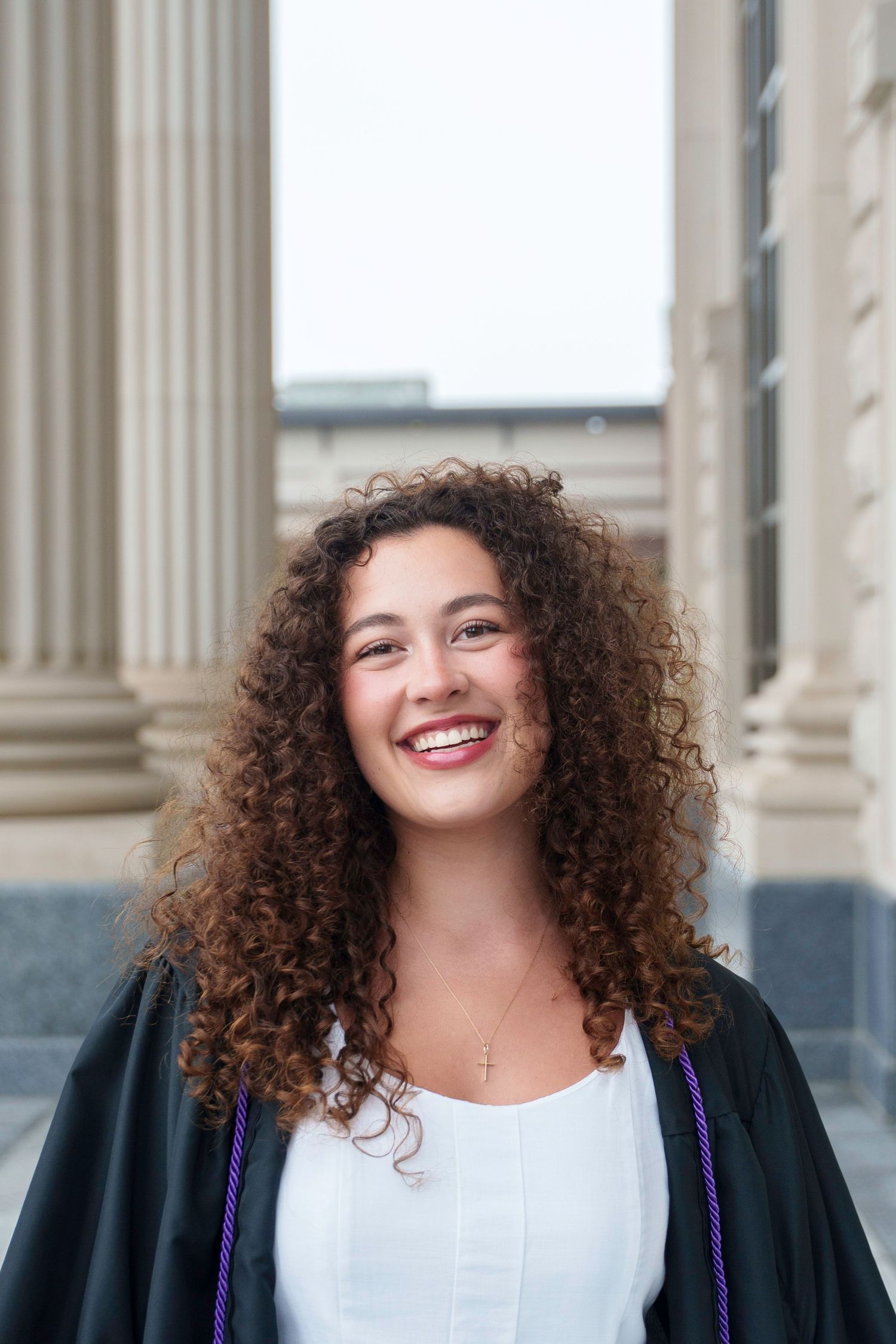 Professional headshots of a person with curly hair wearing a black blazer against a classical building backdrop.
