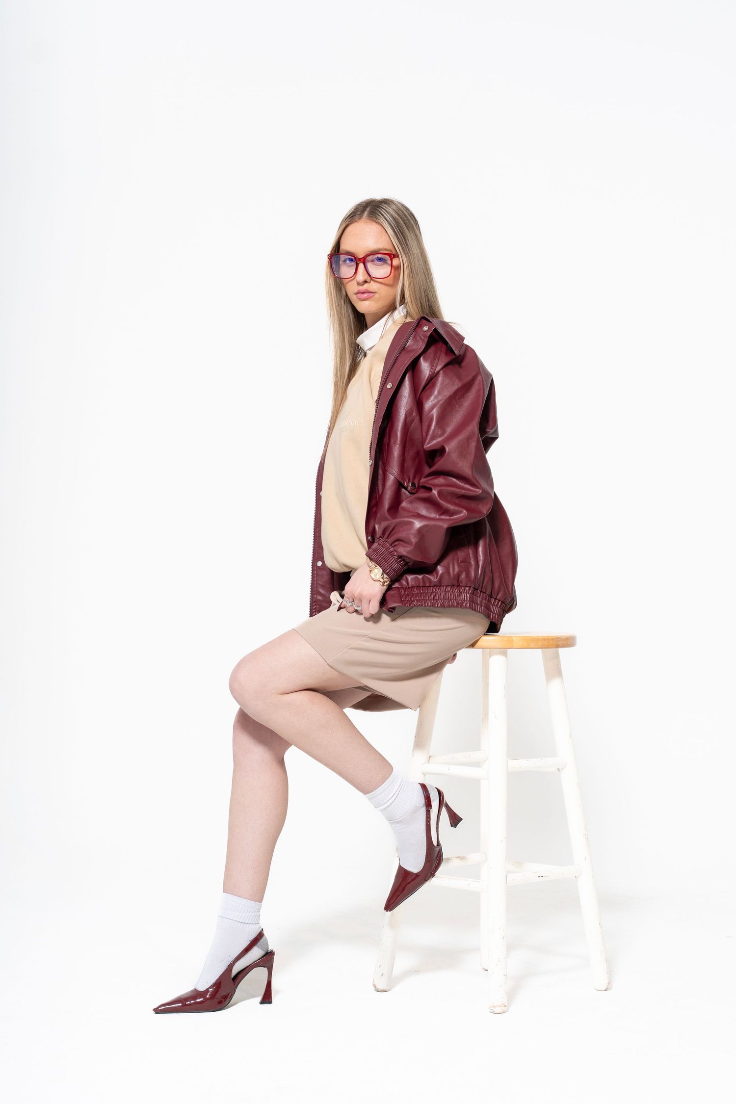 A person in a burgundy leather jacket and beige pants poses on a white chair in three different angles.