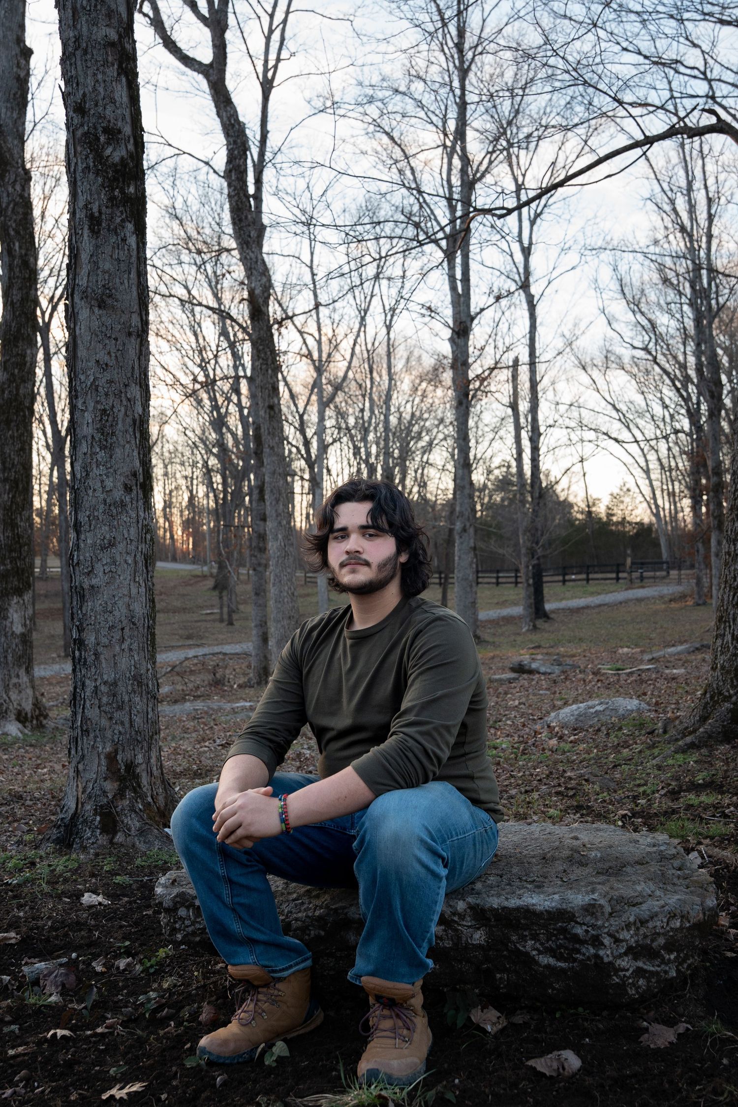 Person sitting on fallen log in wooded area during sunset.