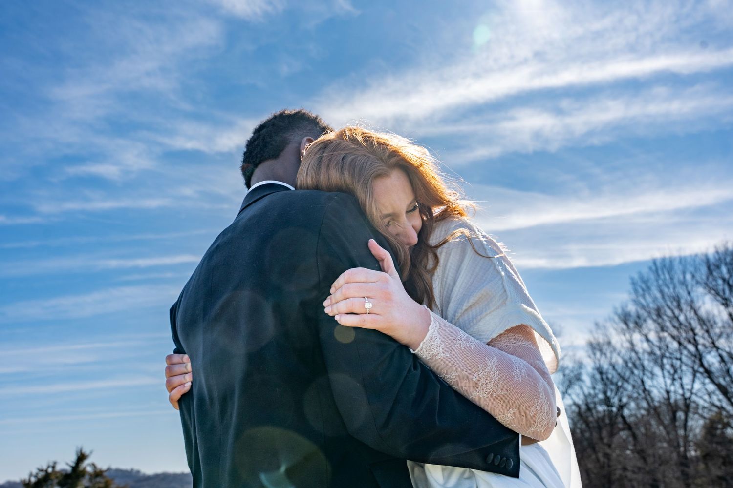 Couple embracing outdoors against blue sky with wispy clouds.