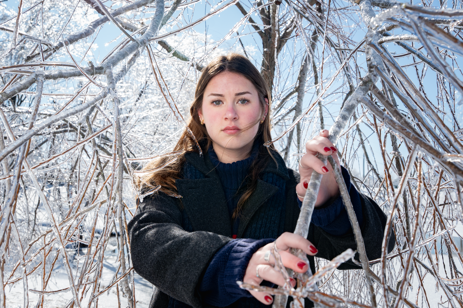 A person in a black coat stands among snow-covered trees in a winter forest setting.