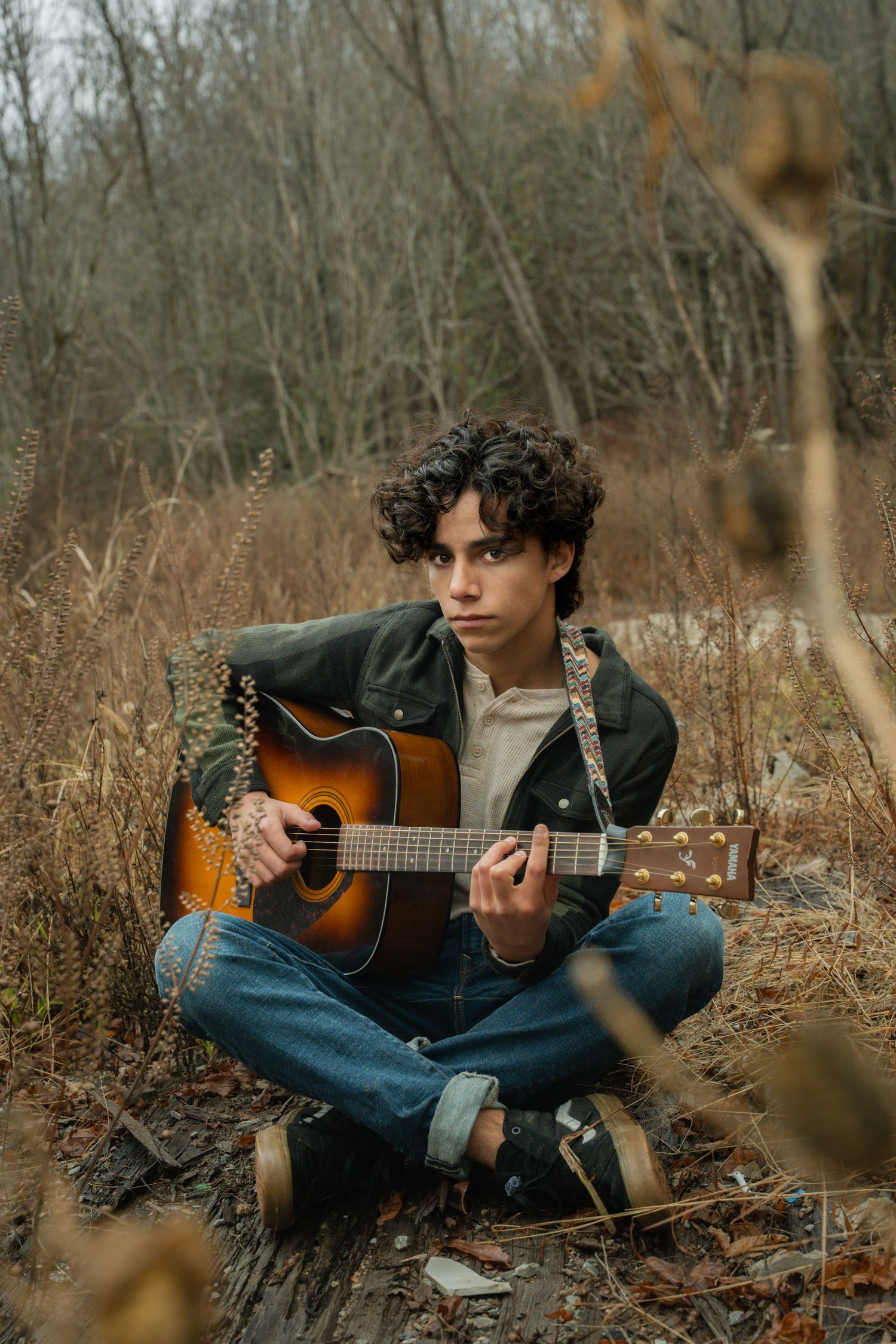 Musician playing acoustic guitar in rustic outdoor setting during fall season.