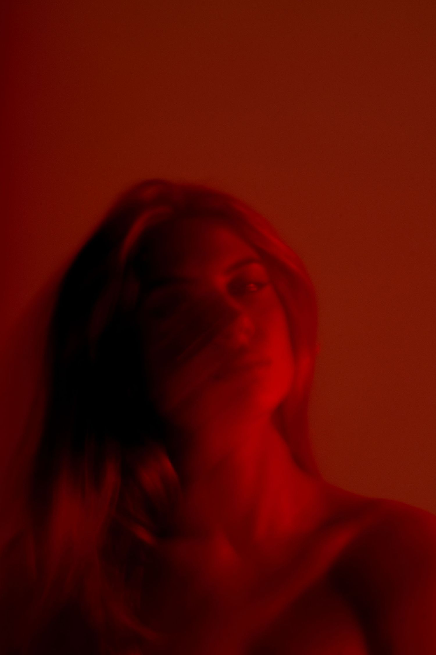 Moody portrait in deep red lighting with dramatic shadows and blur effects.