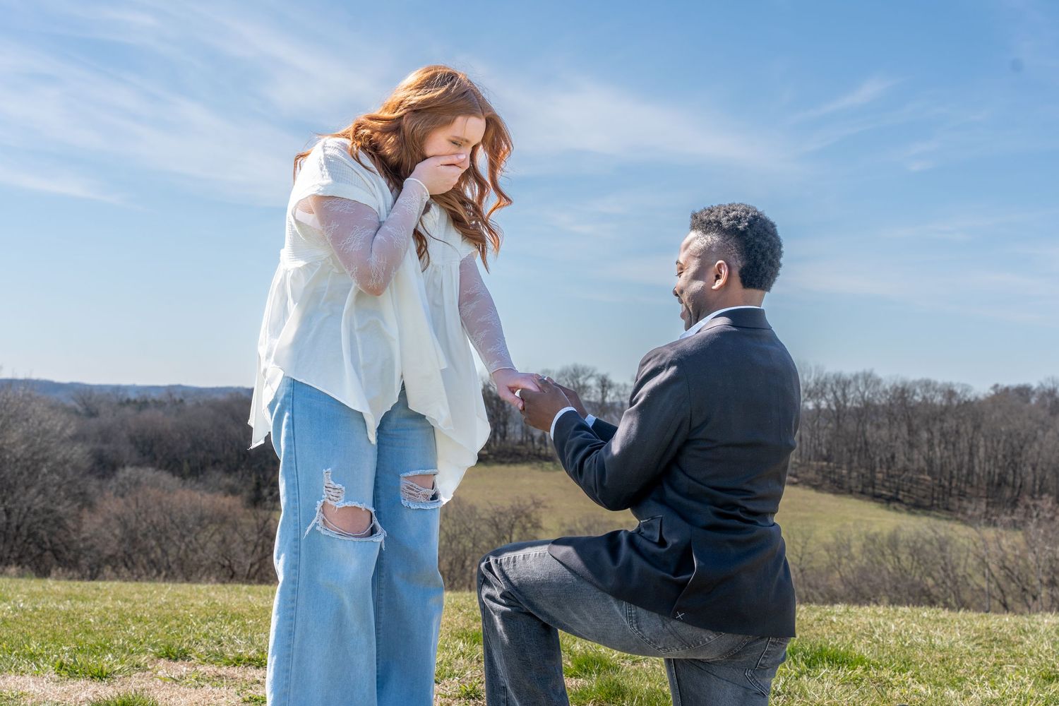 Marriage proposal scene in sunny field with rolling hills in background.