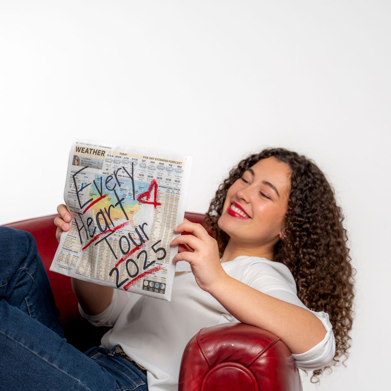 Person with curly hair holding handwritten notes while lounging on red furniture.