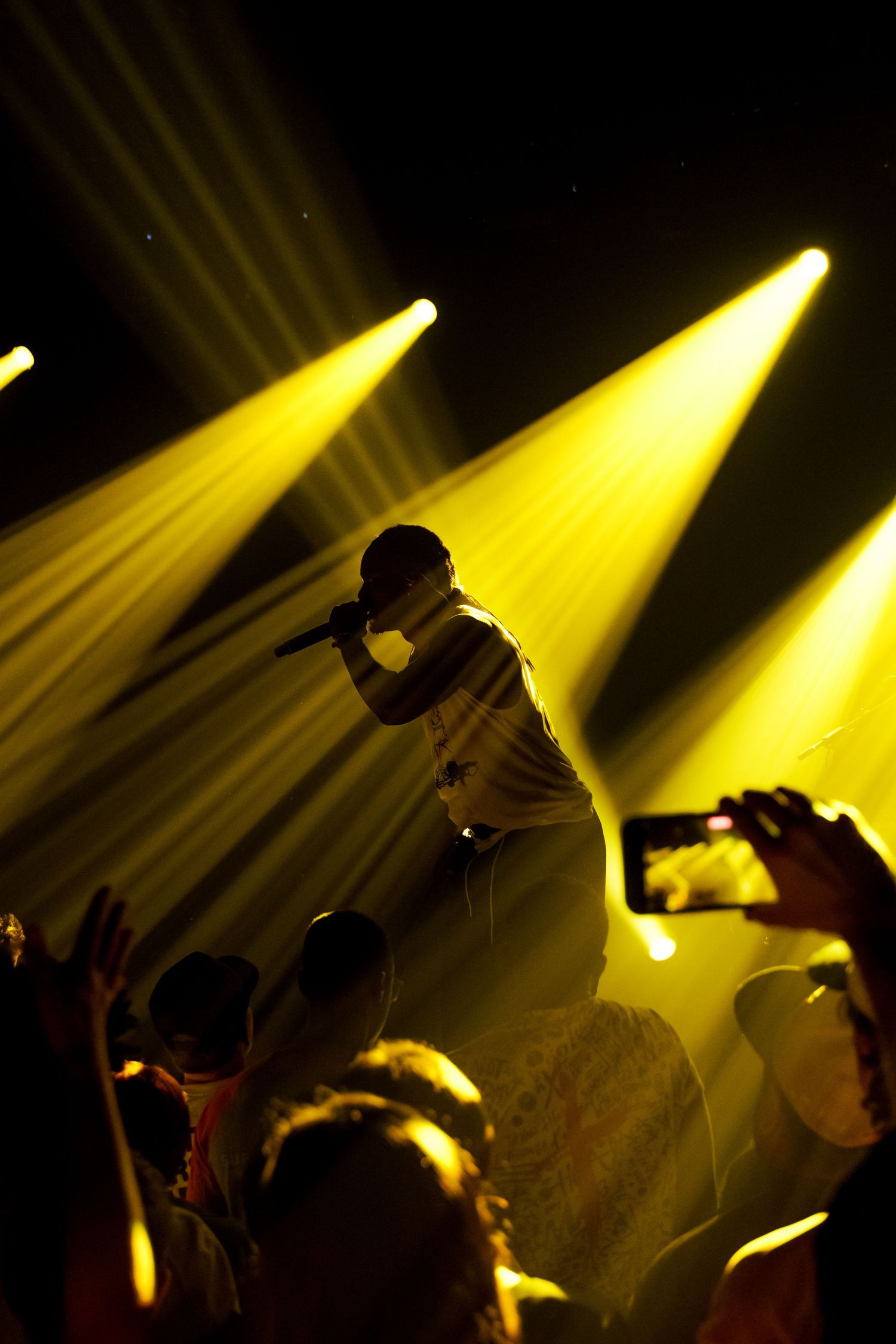 Dramatic concert performance silhouettes against bright yellow spotlights on dark stage.