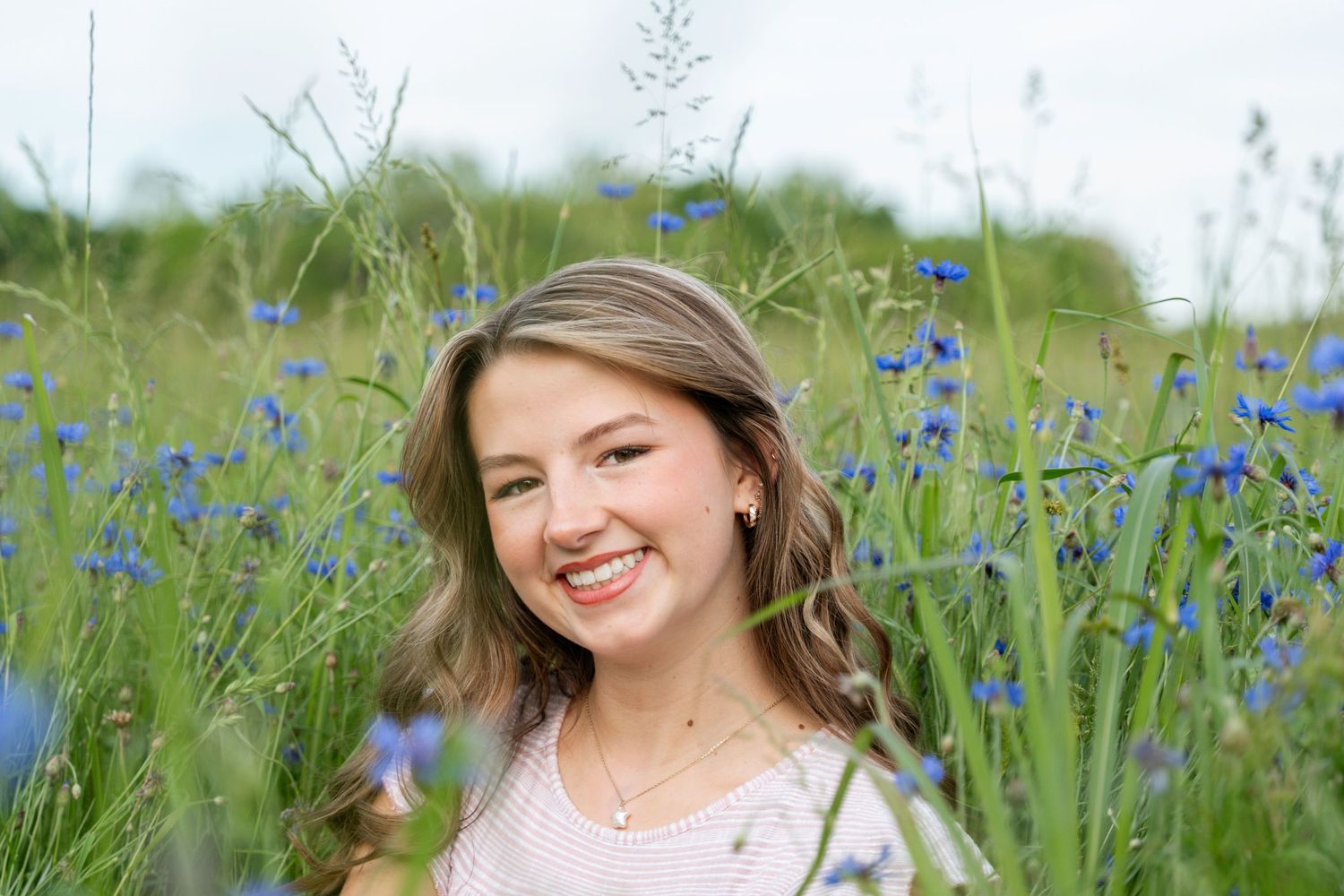 A person poses joyfully in a vibrant meadow filled with blooming blue cornflowers on a sunny summer day.