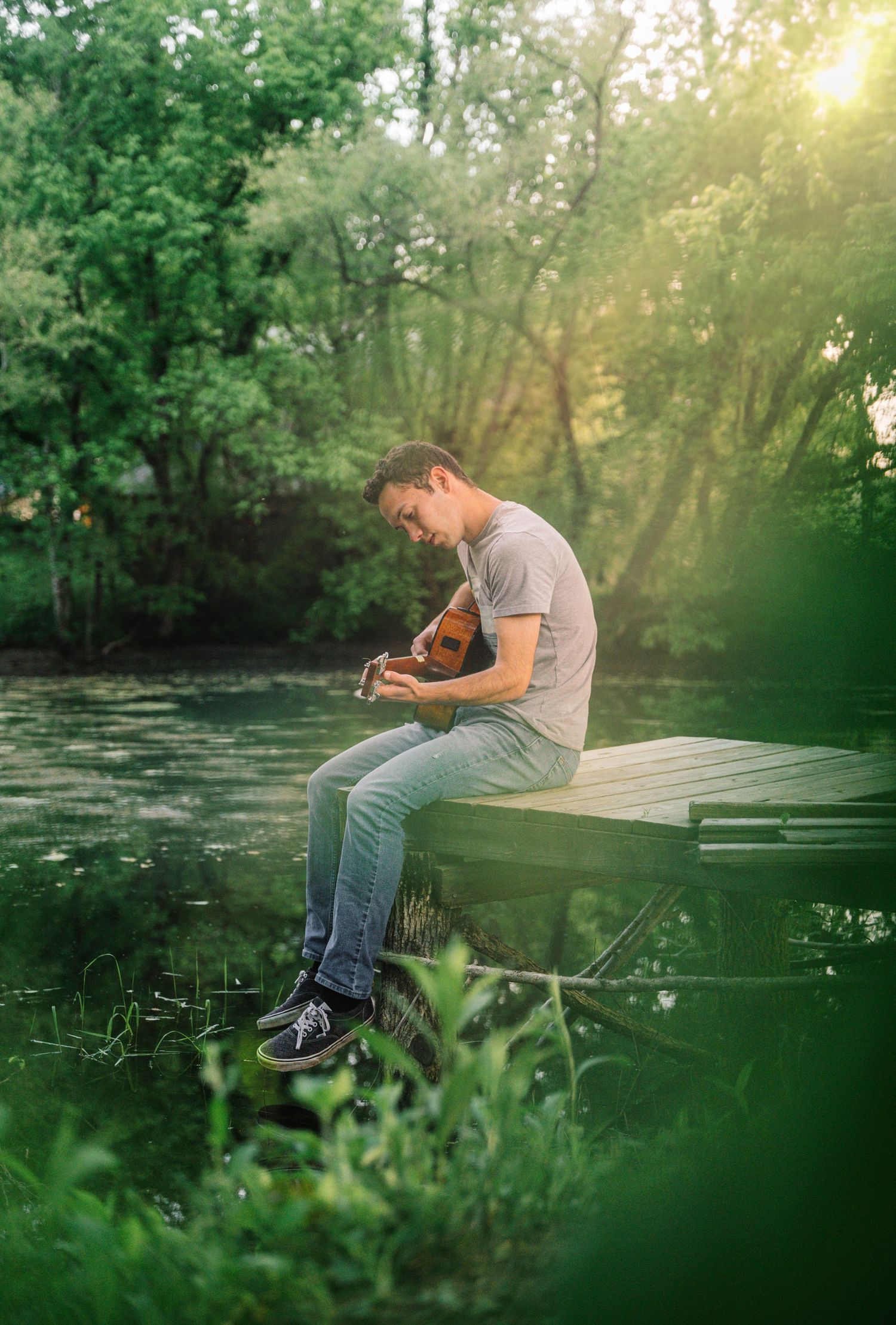 Person sitting on dock by lake playing guitar in serene natural setting during golden hour.