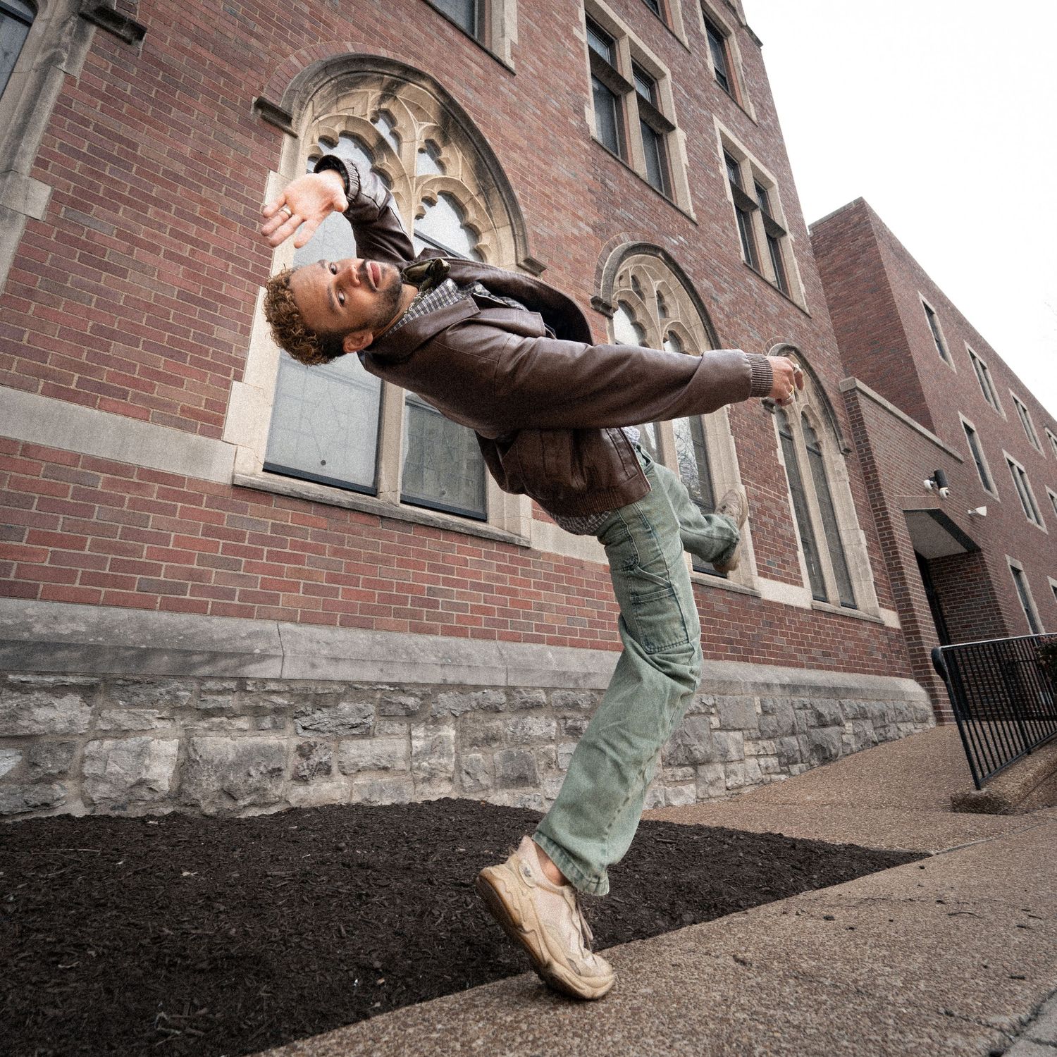 Person dramatically leaning back in front of a historic brick church building on a city sidewalk.