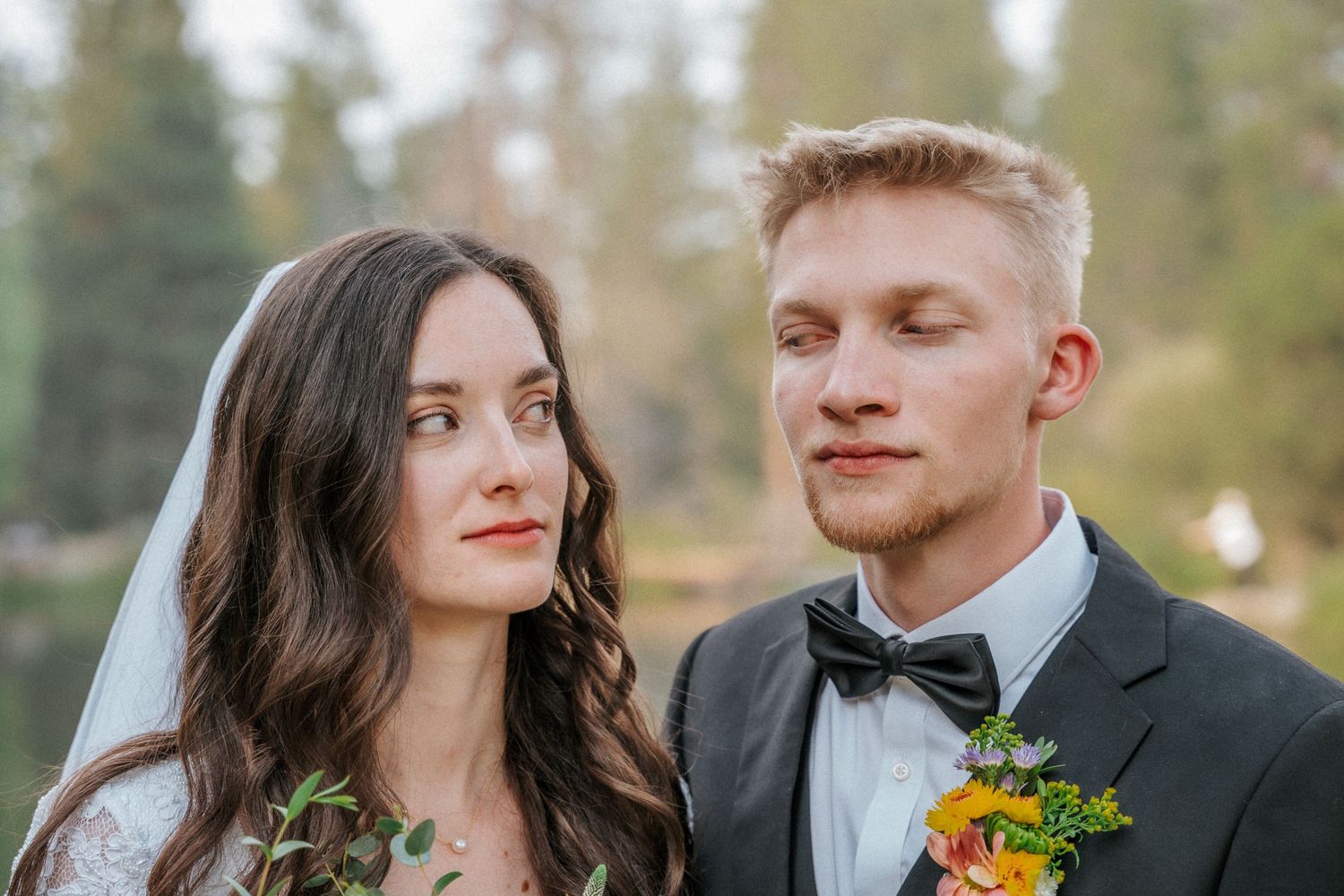 Wedding couple close-up with bright floral bouquet against natural backdrop.