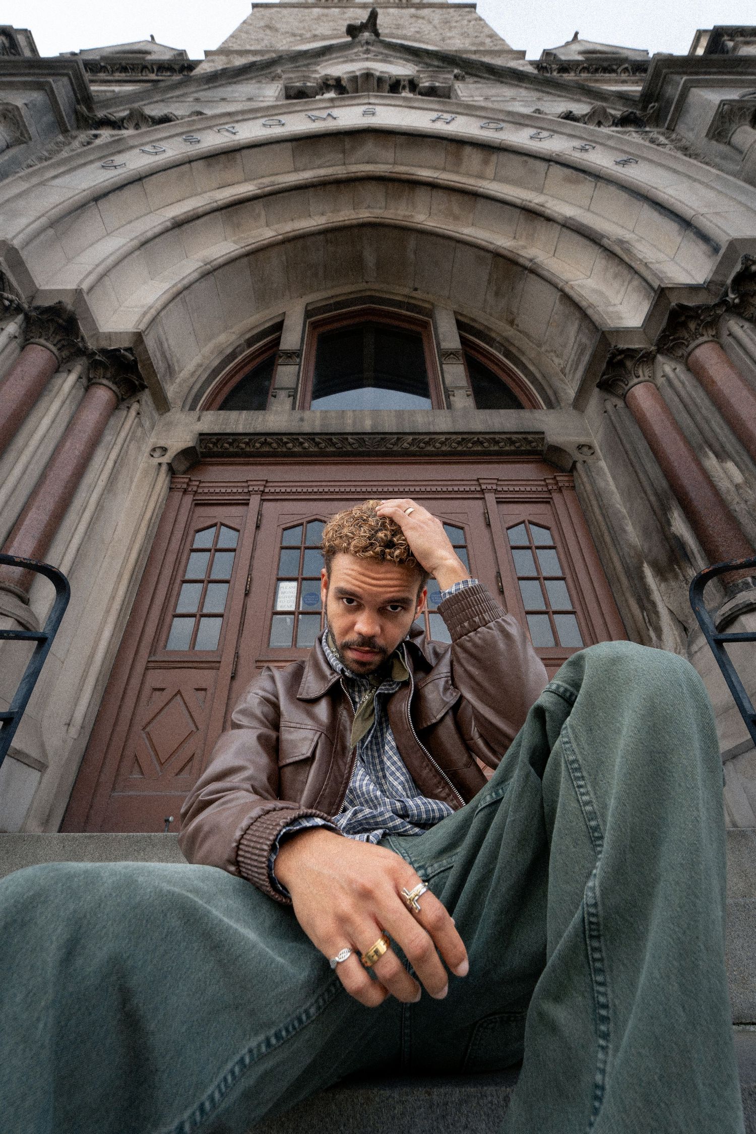 Person sitting on stone steps of ornate historic building in casual green pants against architectural backdrop.