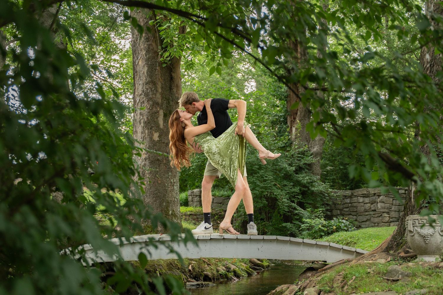 A person walks across a fallen tree trunk bridge in a lush green forest setting.
