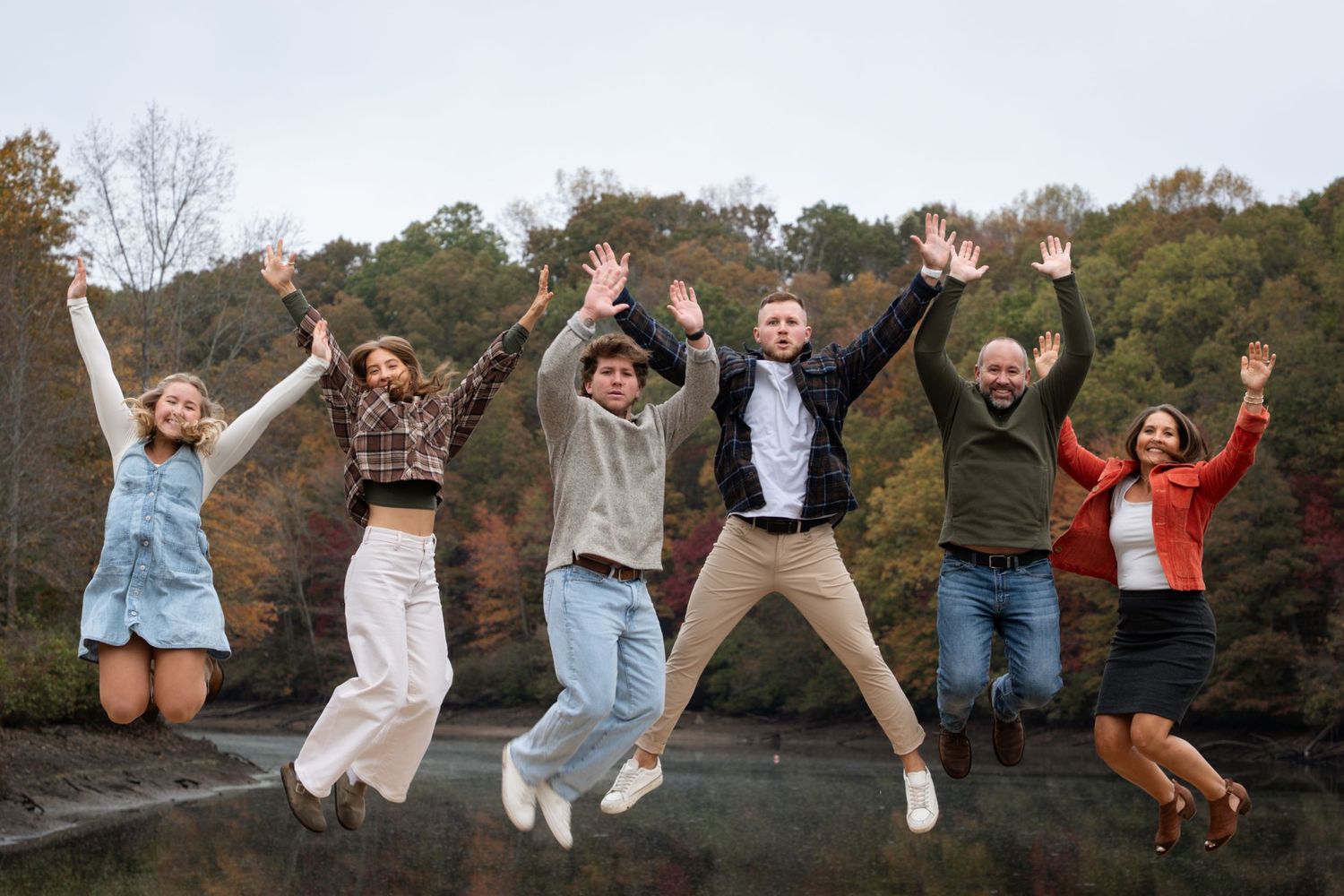 Group of friends jumping together in autumn forest setting with fallen leaves and trees in background.