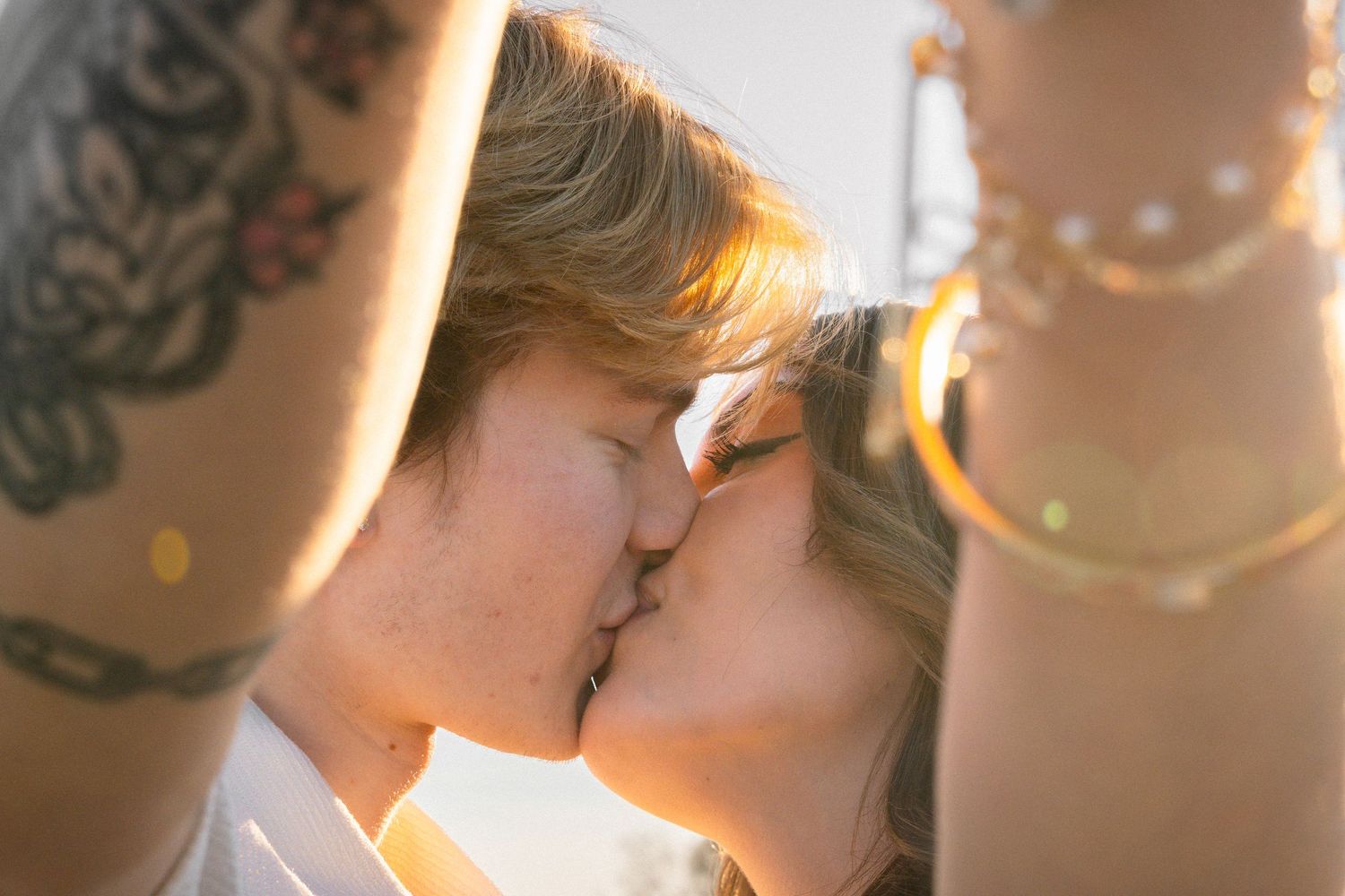 A romantic couple shares a tender kiss in golden sunlight with bokeh effects in the background.