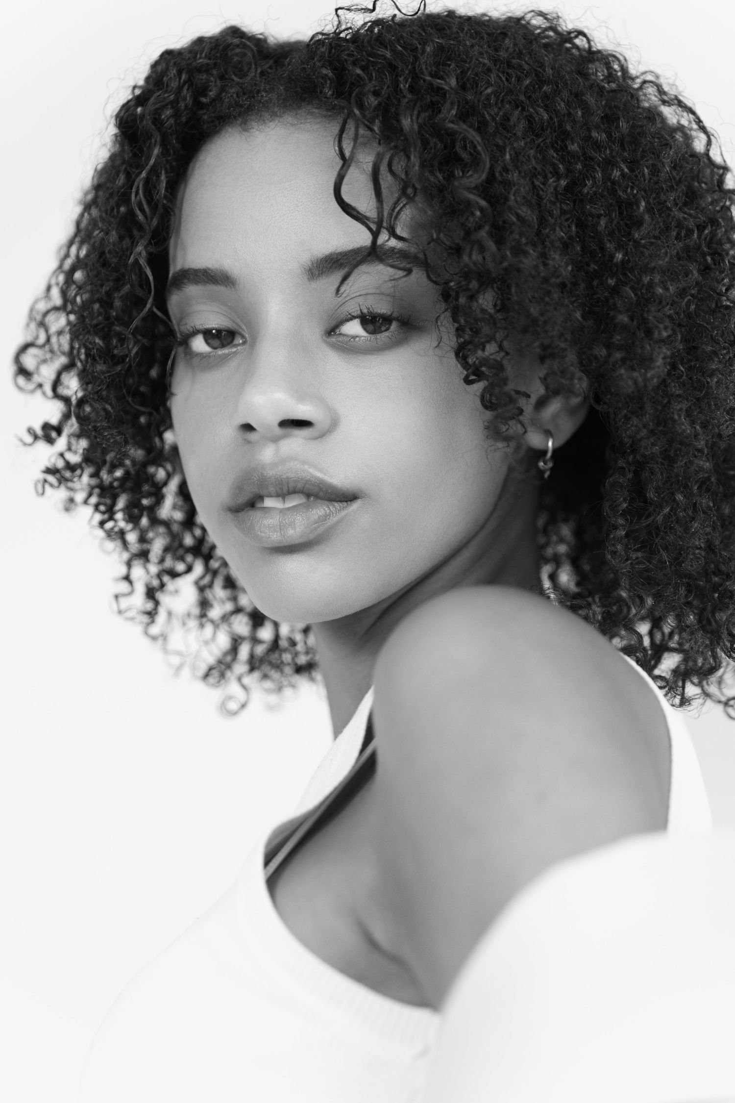 Black and white portrait of a young woman with natural curly hair wearing an off-shoulder white top.