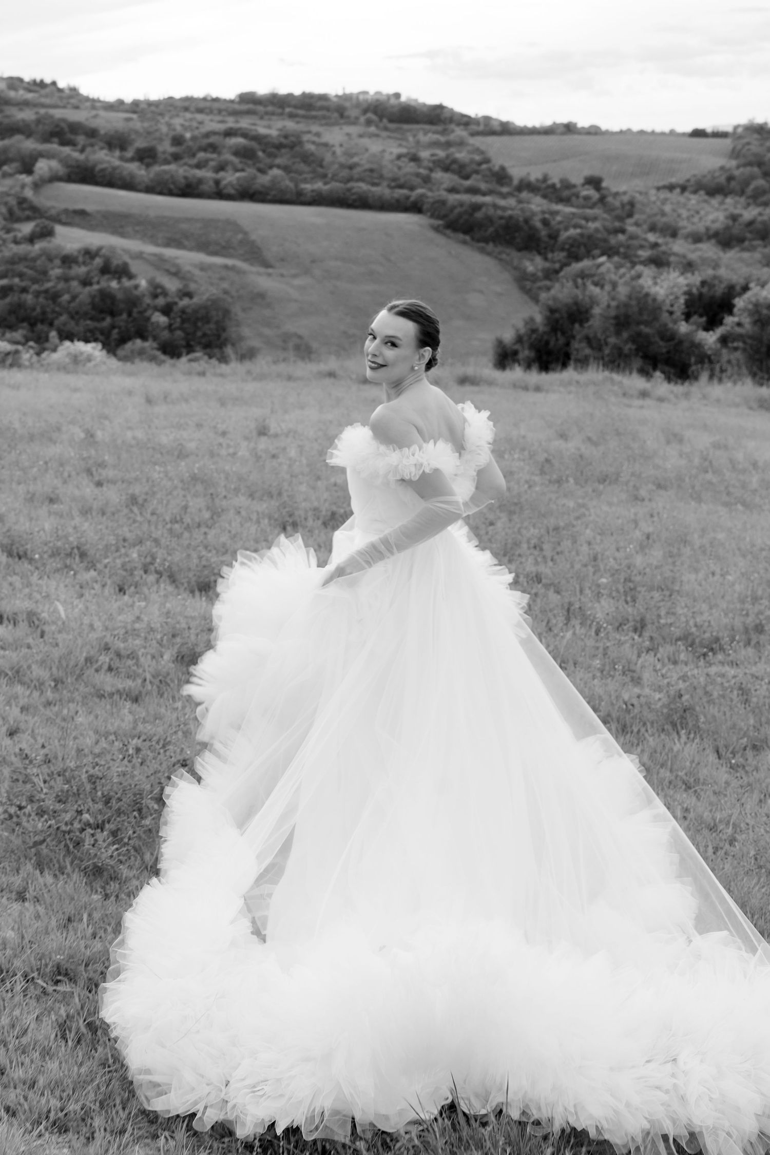 Bride twirls in a dramatic ruffled tulle gown in a sweeping black and white Tuscan countryside portrait.