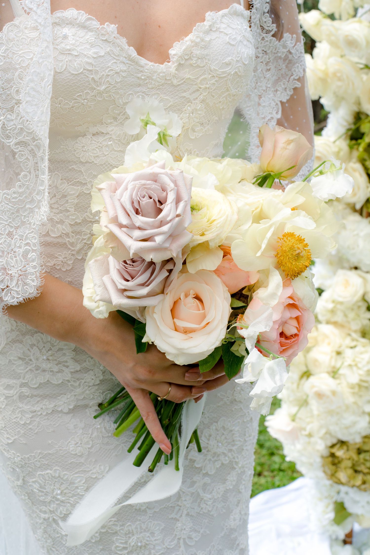 Bride in lace wedding dress holds a romantic bouquet of mauve, peach, and cream roses.