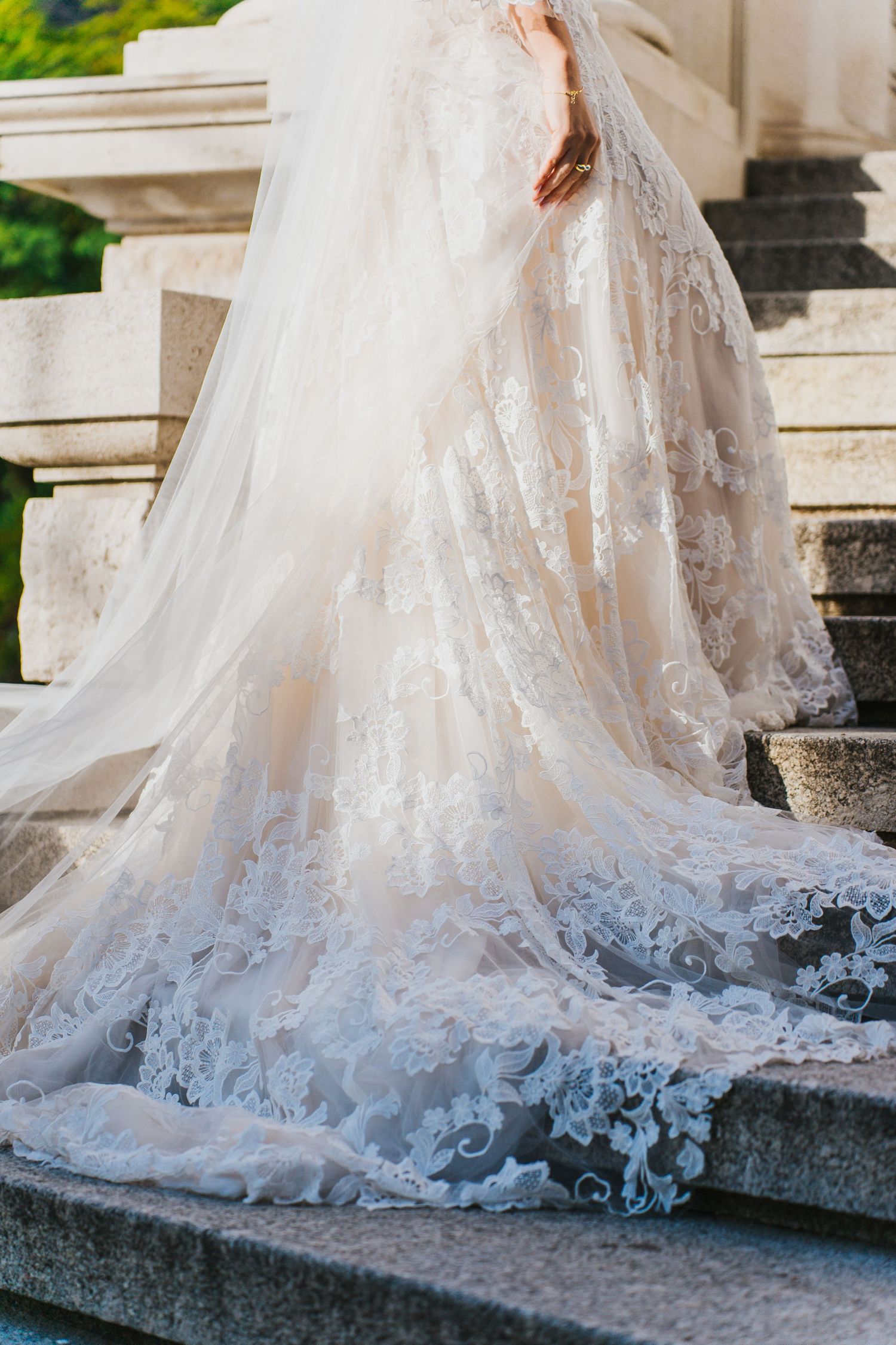 Close-up of bride in ornate lace wedding gown with long train cascading down stone steps.