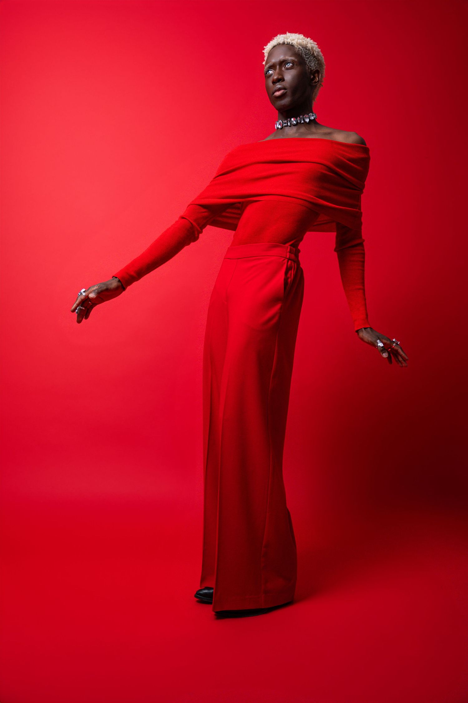 Tall Black woman in elegant red off-shoulder gown with silver jewelry posing on red background.