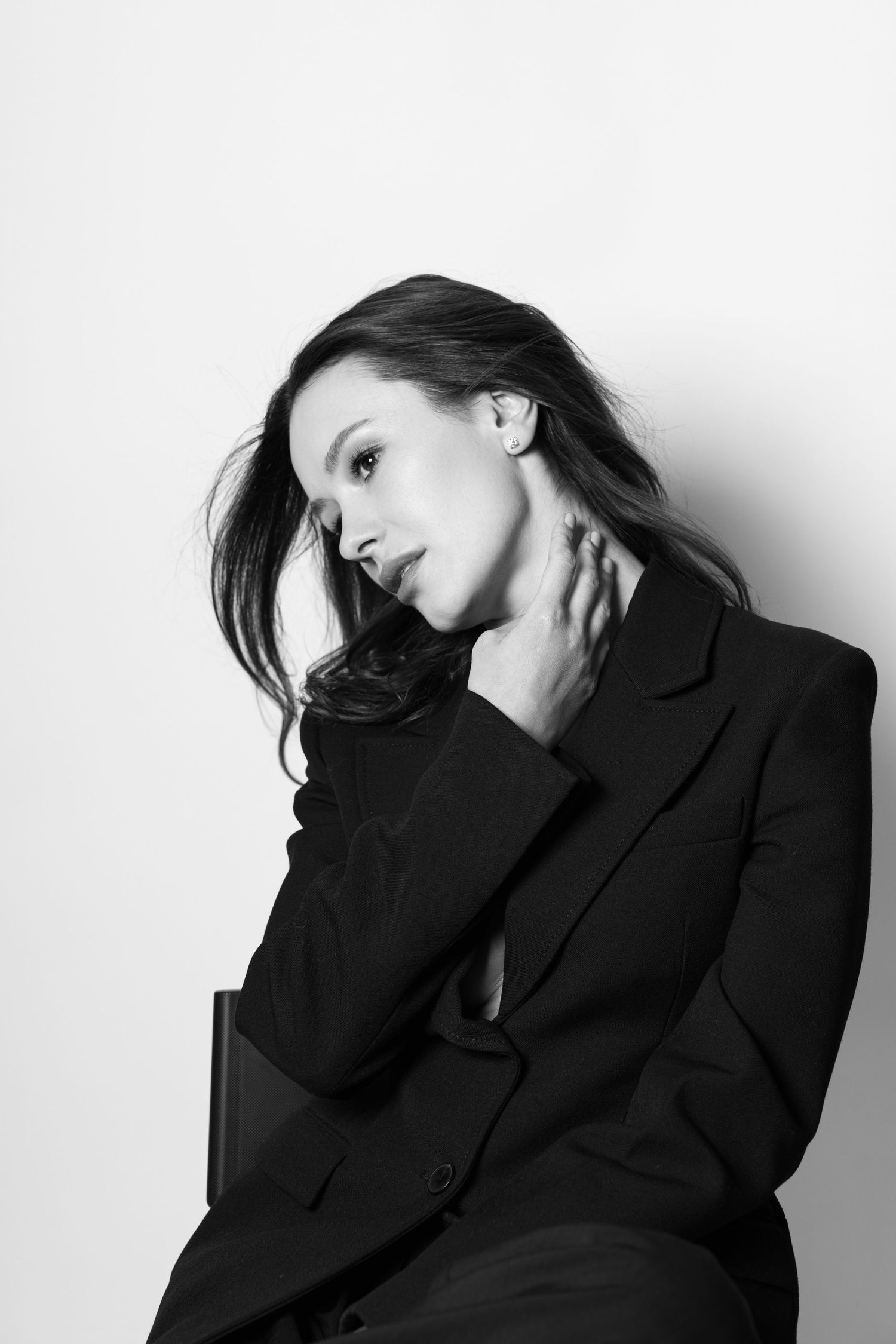 Black and white portrait of elegant woman in black blazer sitting against white background.