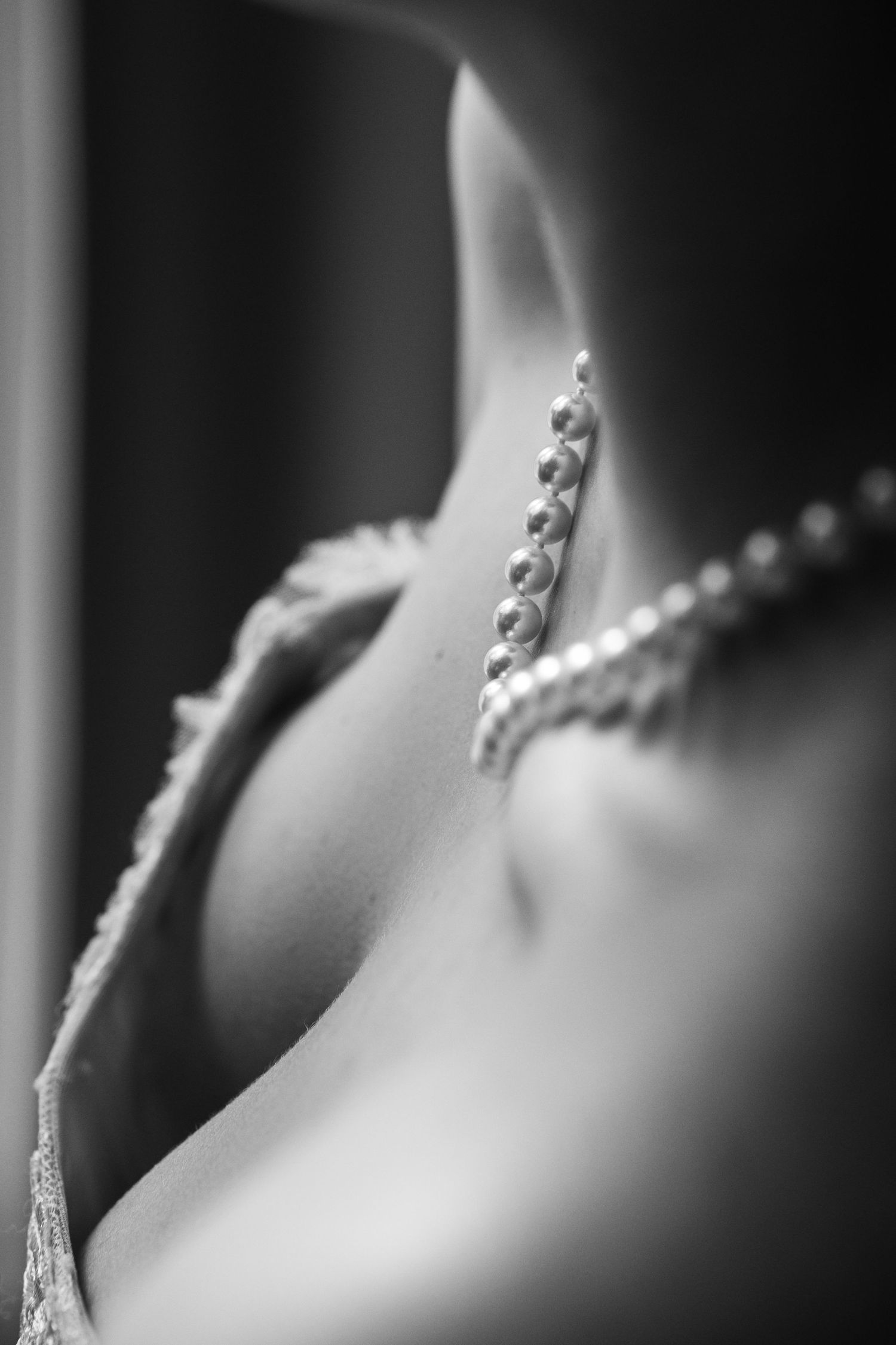 Close-up black and white detail of pearl button closure on back of elegant lace bridal gown.