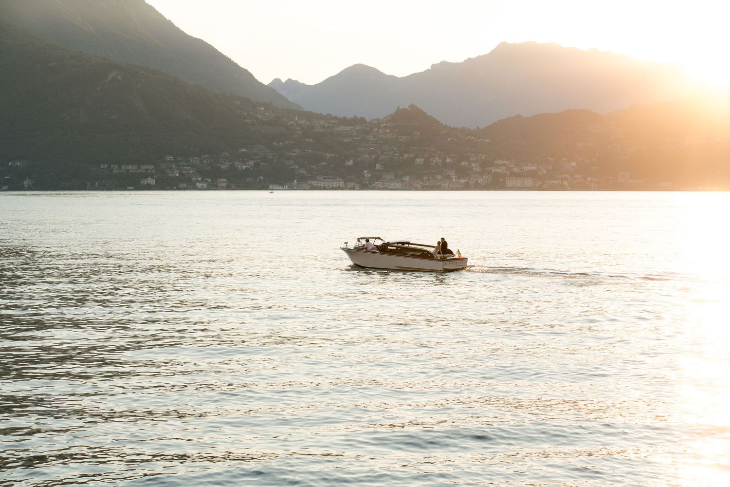 A motorboat cruises on calm lake waters at golden sunset with silhouetted mountains in the background.