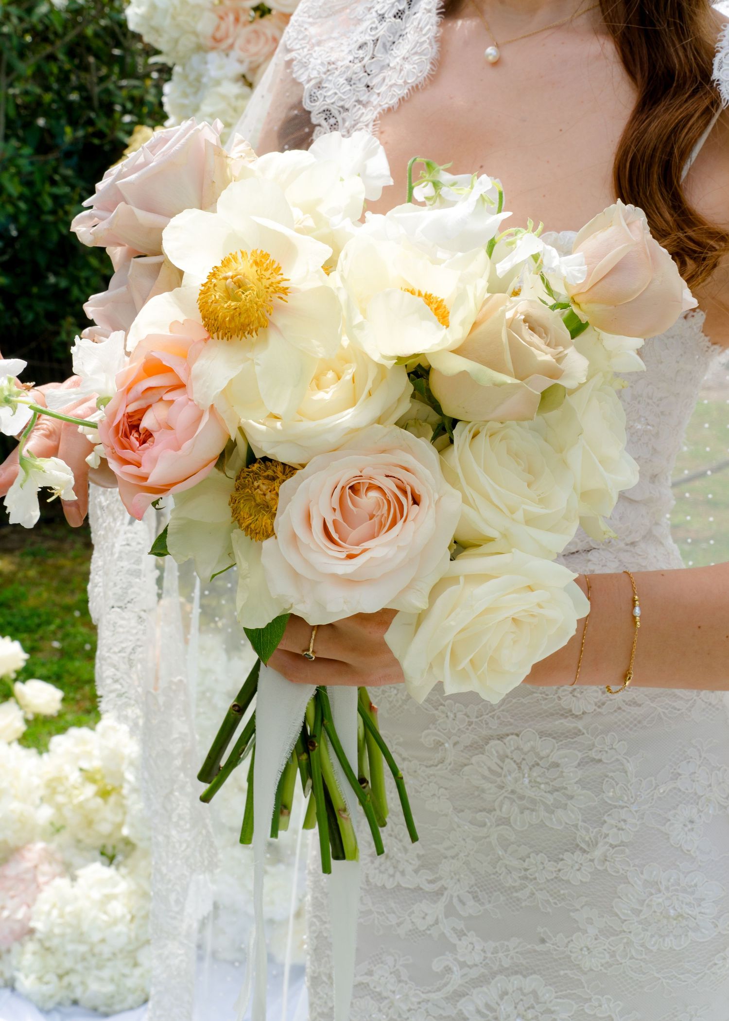 Bride holds a romantic bouquet of cream roses, peonies, and peach blooms in a lace wedding gown.