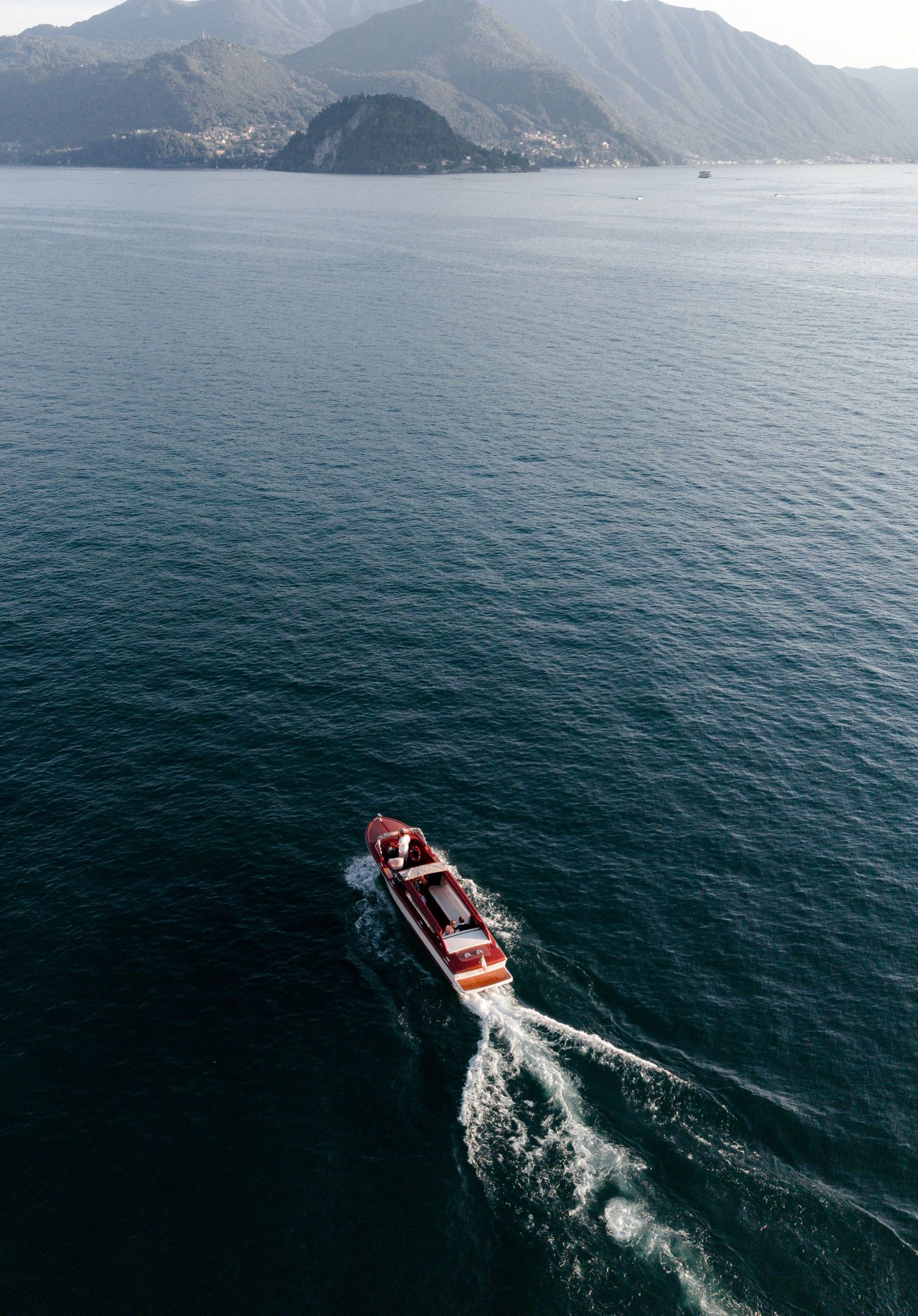 Aerial view of a classic wooden speedboat cruising on a deep blue alpine lake with mountain backdrop.