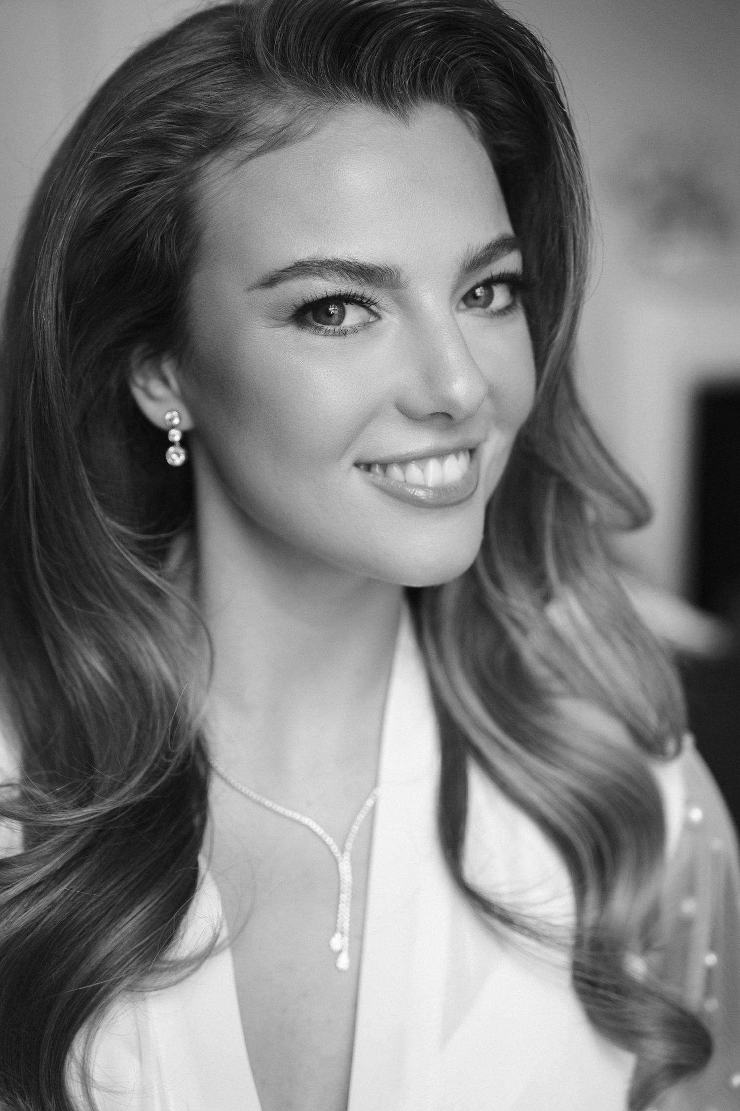 Elegant bride smiles in black and white portrait wearing diamond earrings and necklace.