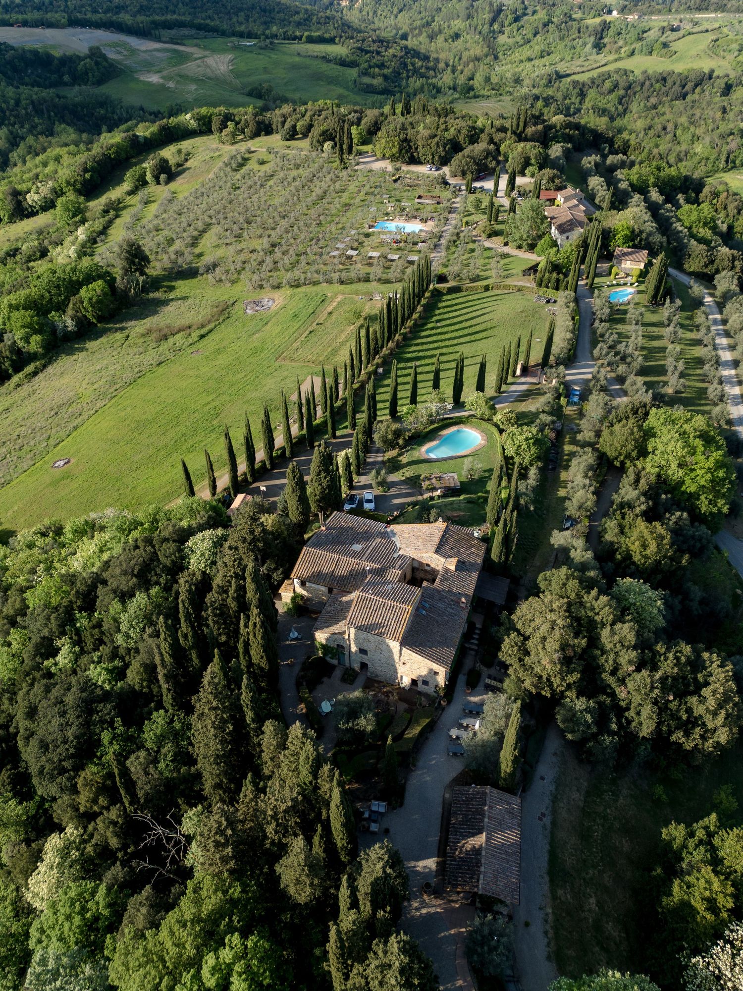 Aerial perspective of a beautiful Tuscan villa with formal gardens, cypress trees, and swimming pool.