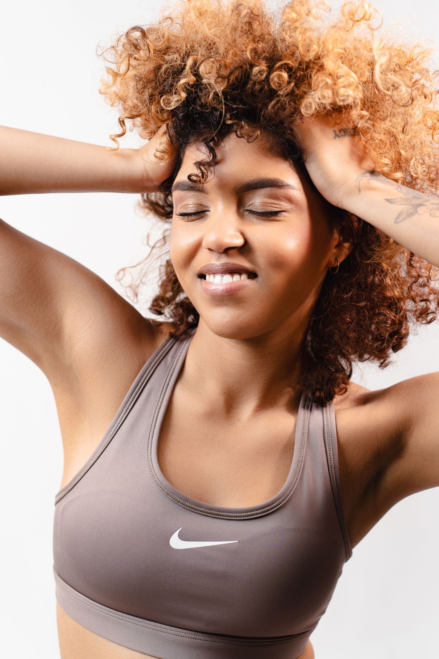 Close-up of smiling woman with curly auburn hair in Nike sports bra with eyes closed.