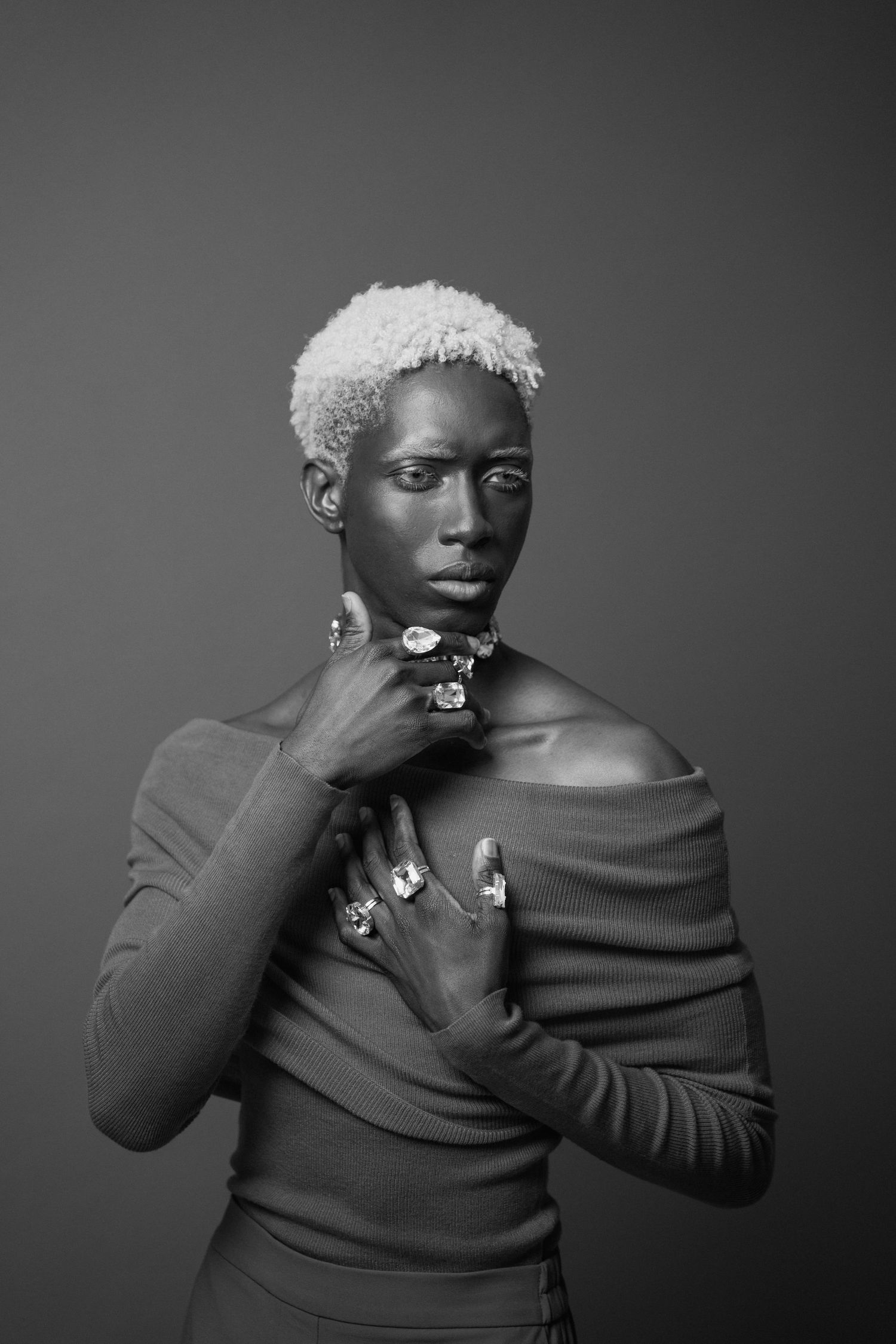 Elegant black and white portrait of woman with blonde cropped hair in off-shoulder top with statement jewelry.
