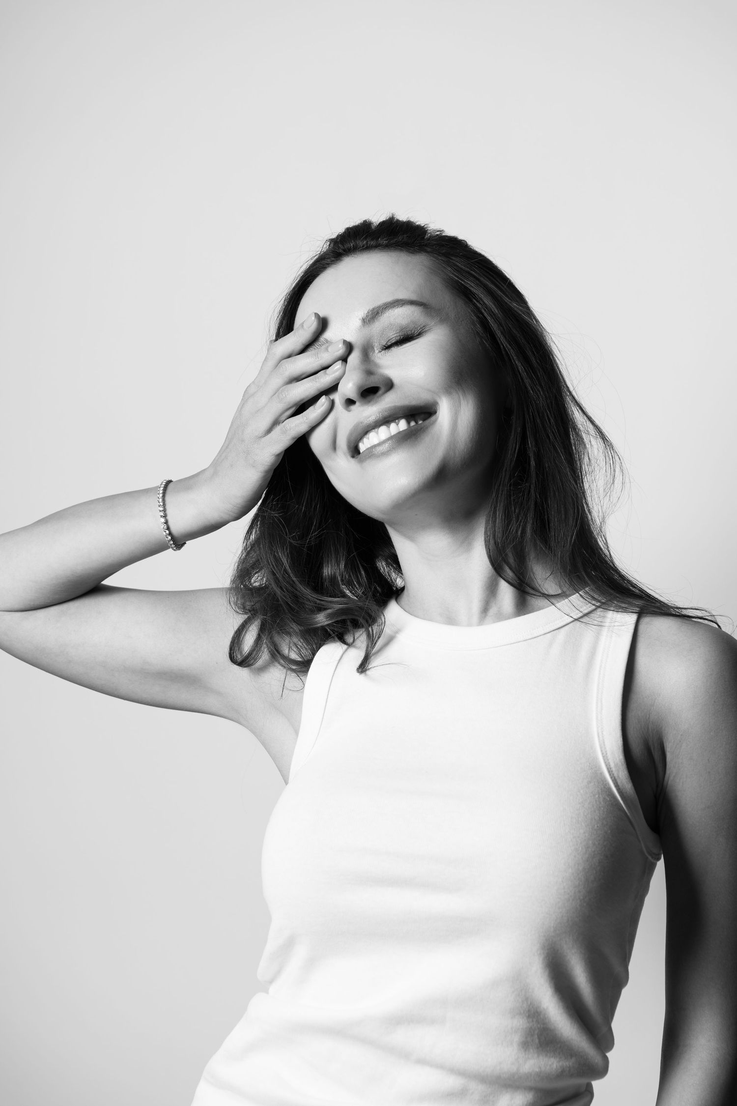 Black and white portrait of a smiling brunette woman covering her eye with her hand.