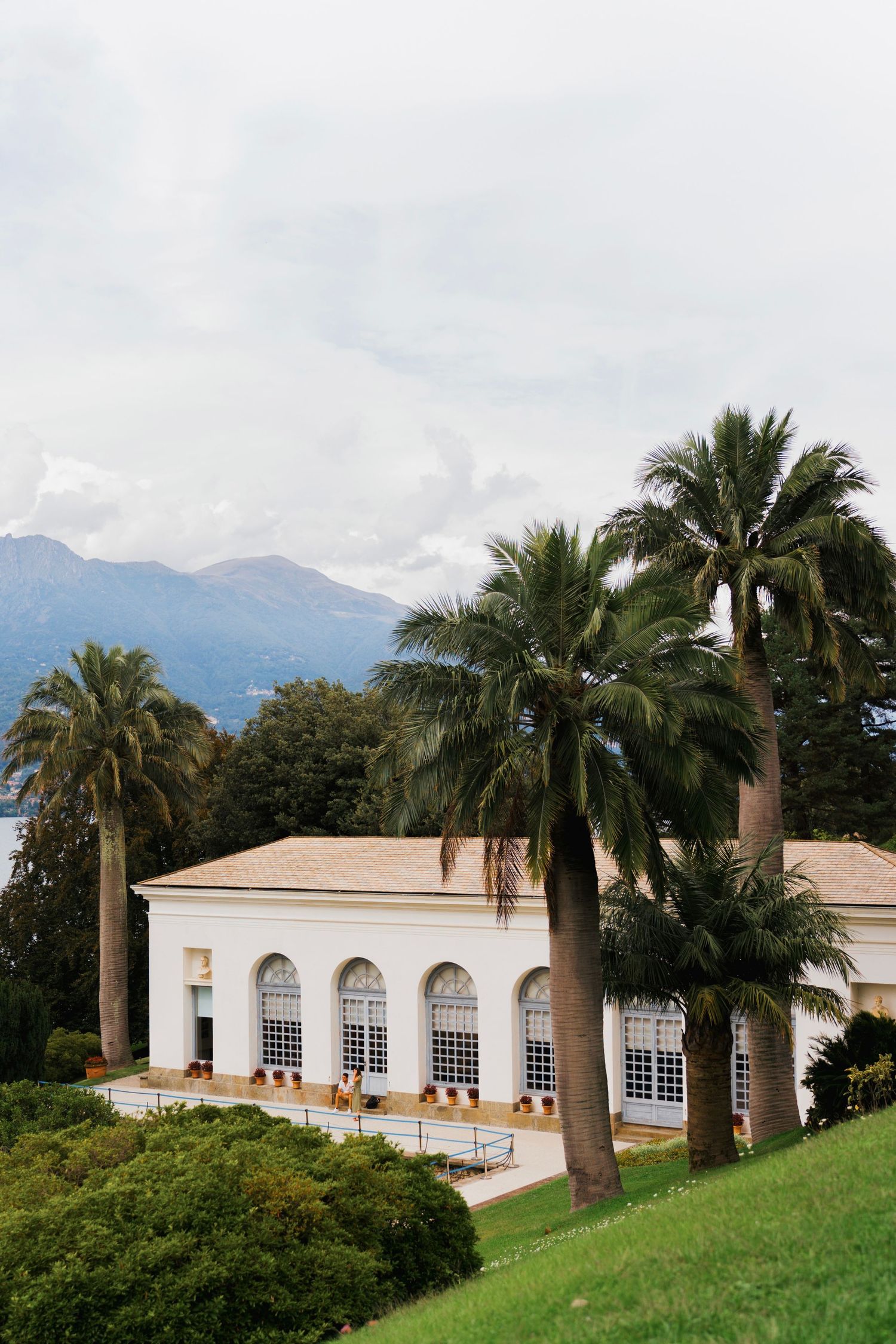Elegant white villa with arched windows surrounded by palm trees and mountain backdrop.