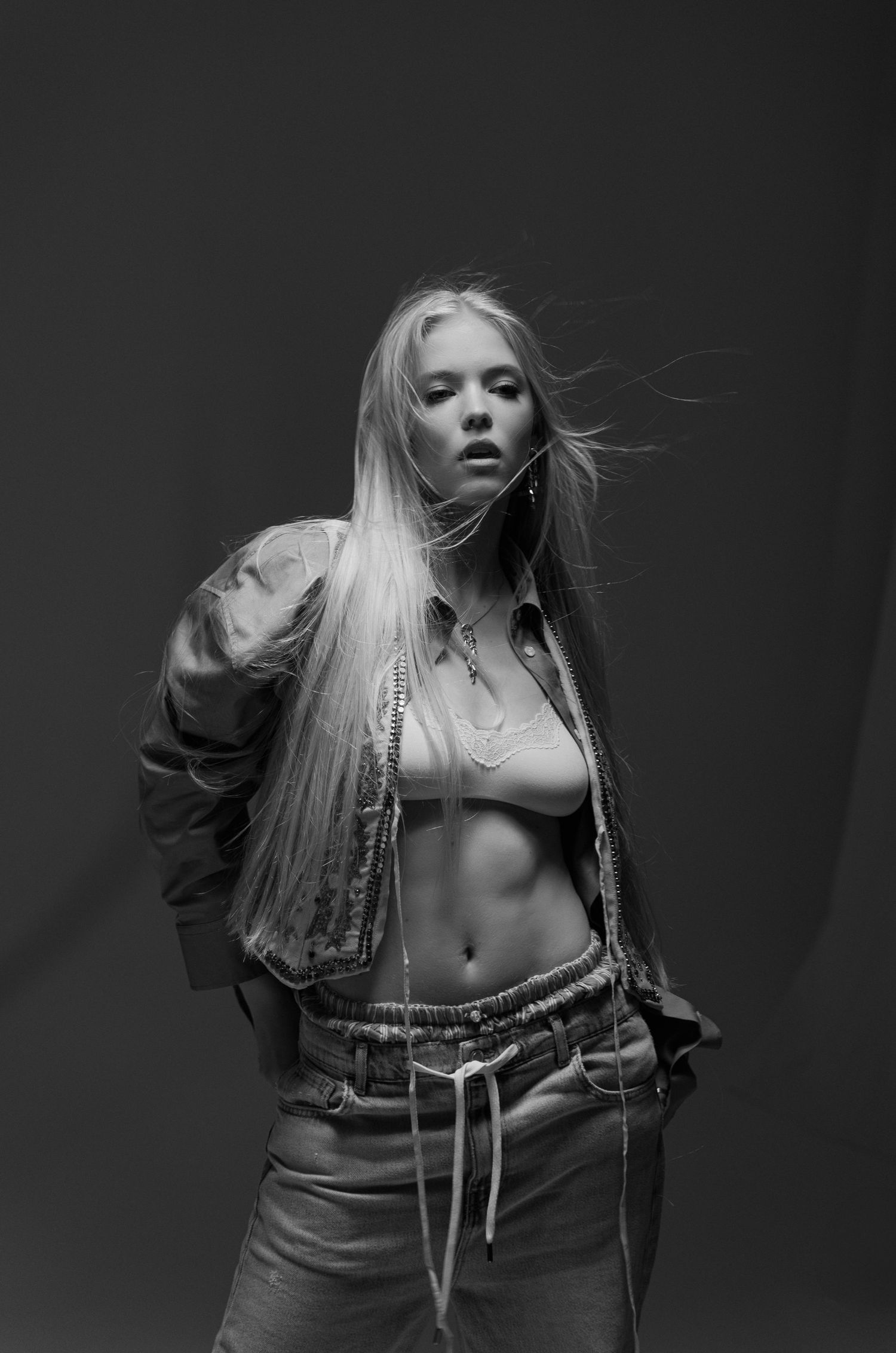 Black and white fashion portrait of a blonde woman with windswept hair in open jacket.