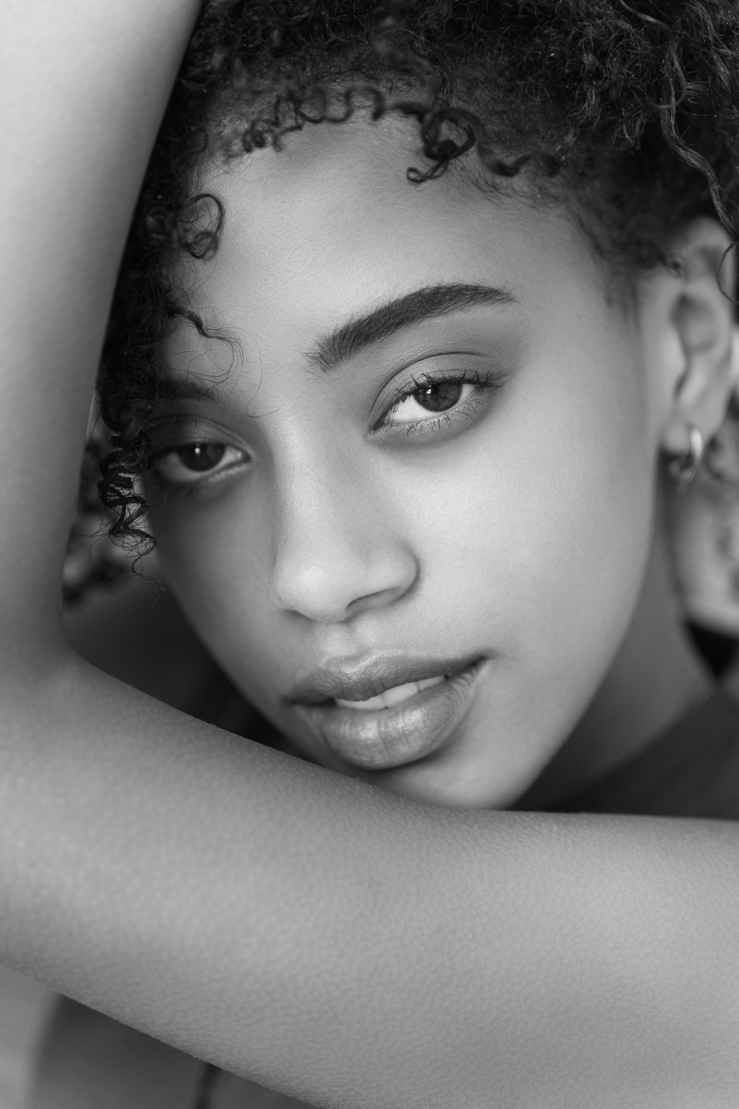 Black and white portrait of young woman with curly hair, arm raised gracefully beside her face.