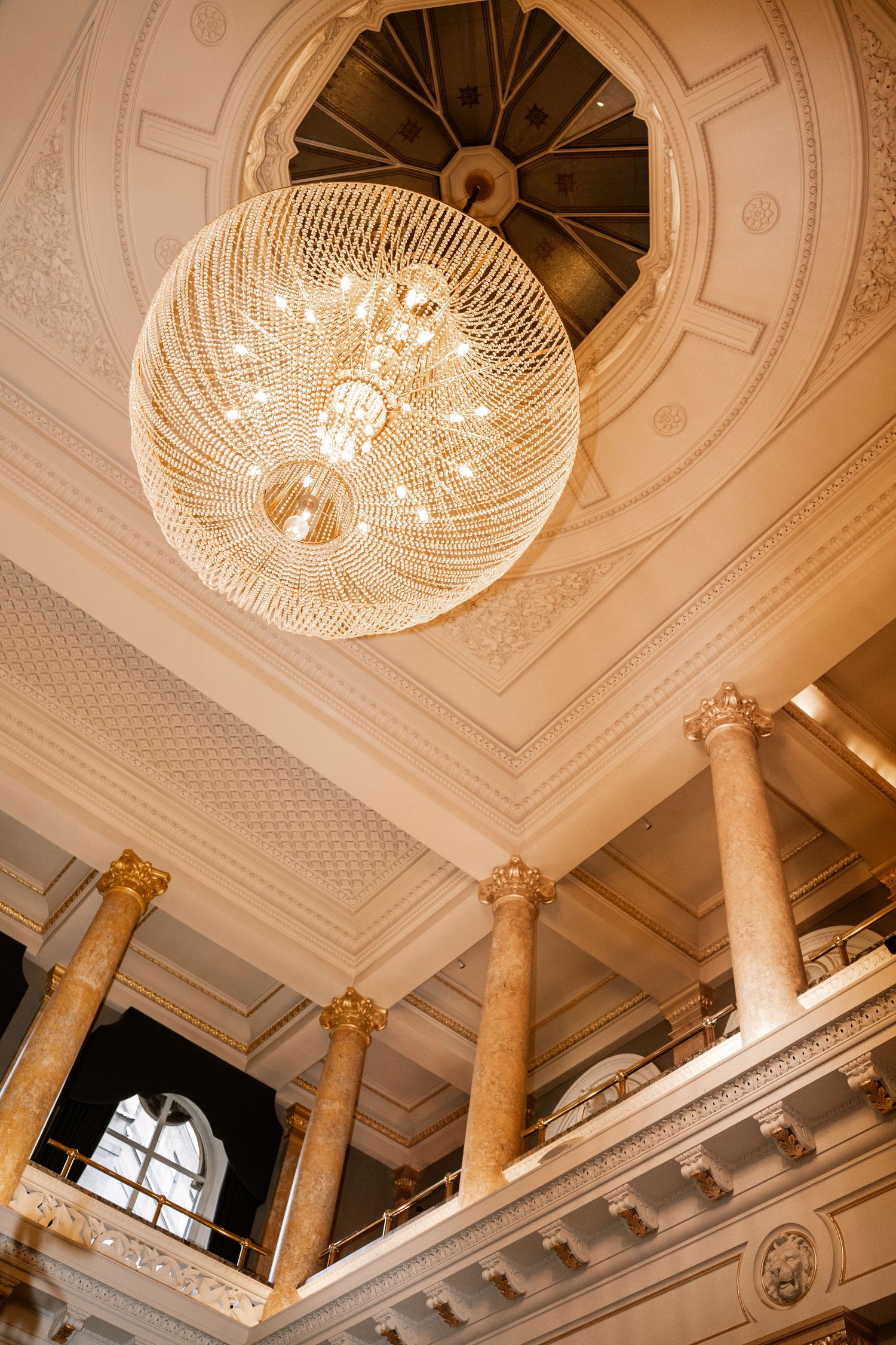 Elegant grand ballroom ceiling with spherical crystal chandelier and ornate gold columns.