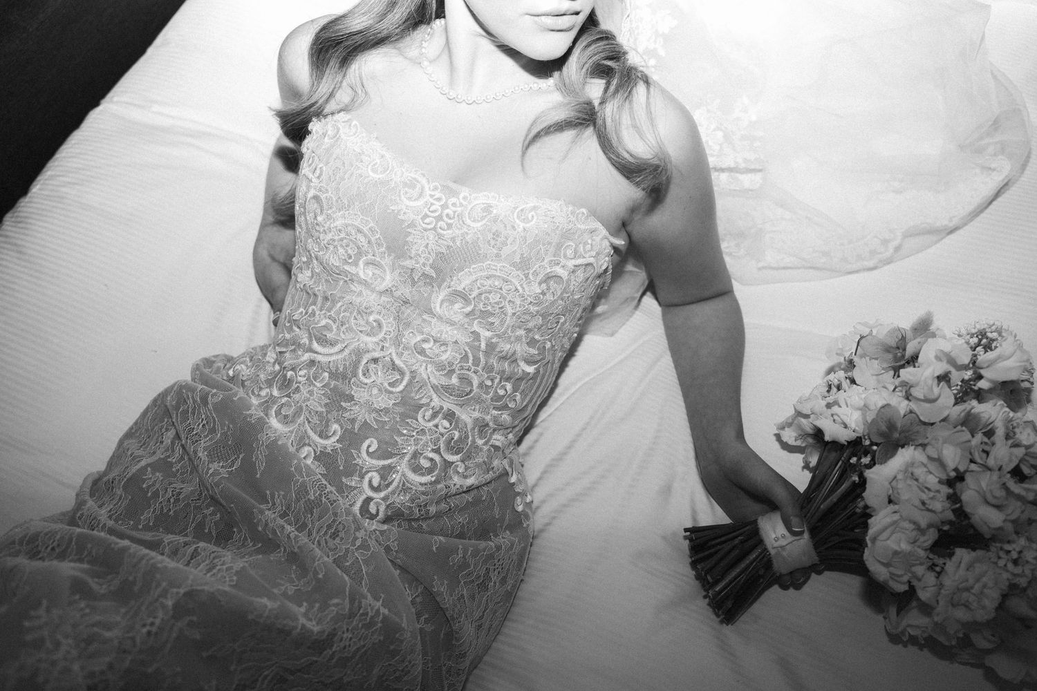 Black and white artistic photo of bride in lace wedding gown holding bouquet while reclining.