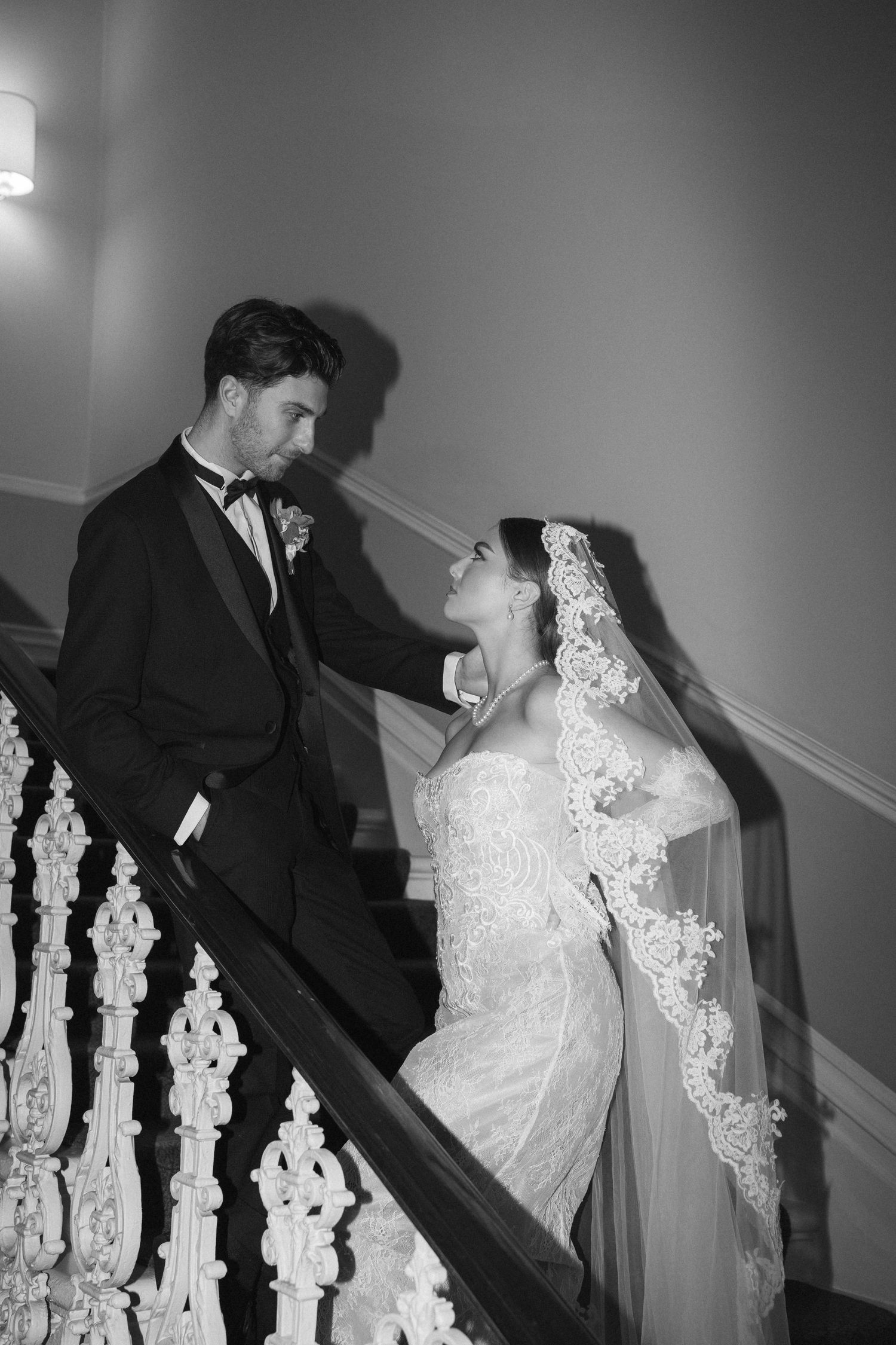 Elegant black and white wedding portrait of couple on decorative staircase with bride in lace veil.