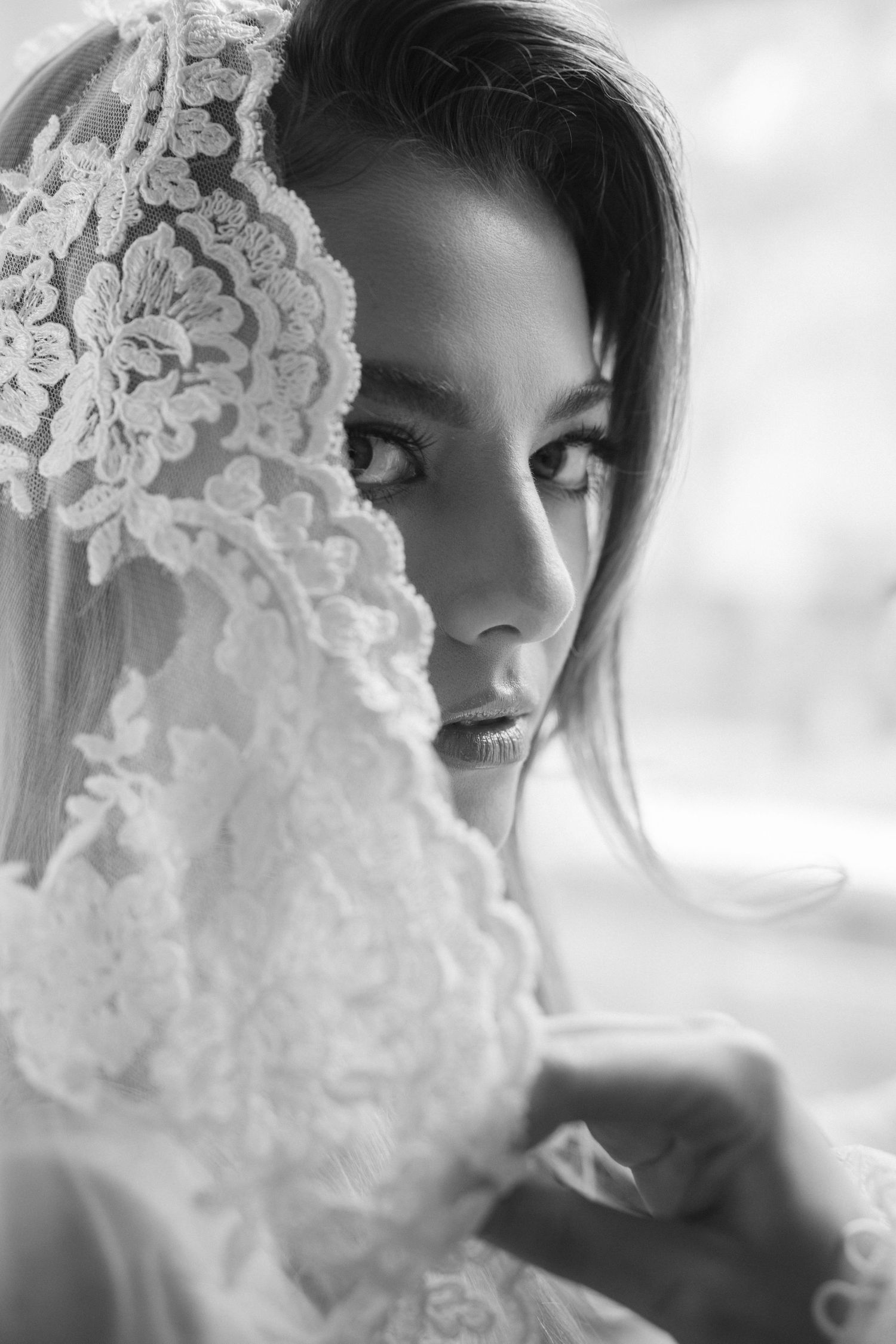 Black and white close-up portrait of a bride with intricate lace veil draped over her face.