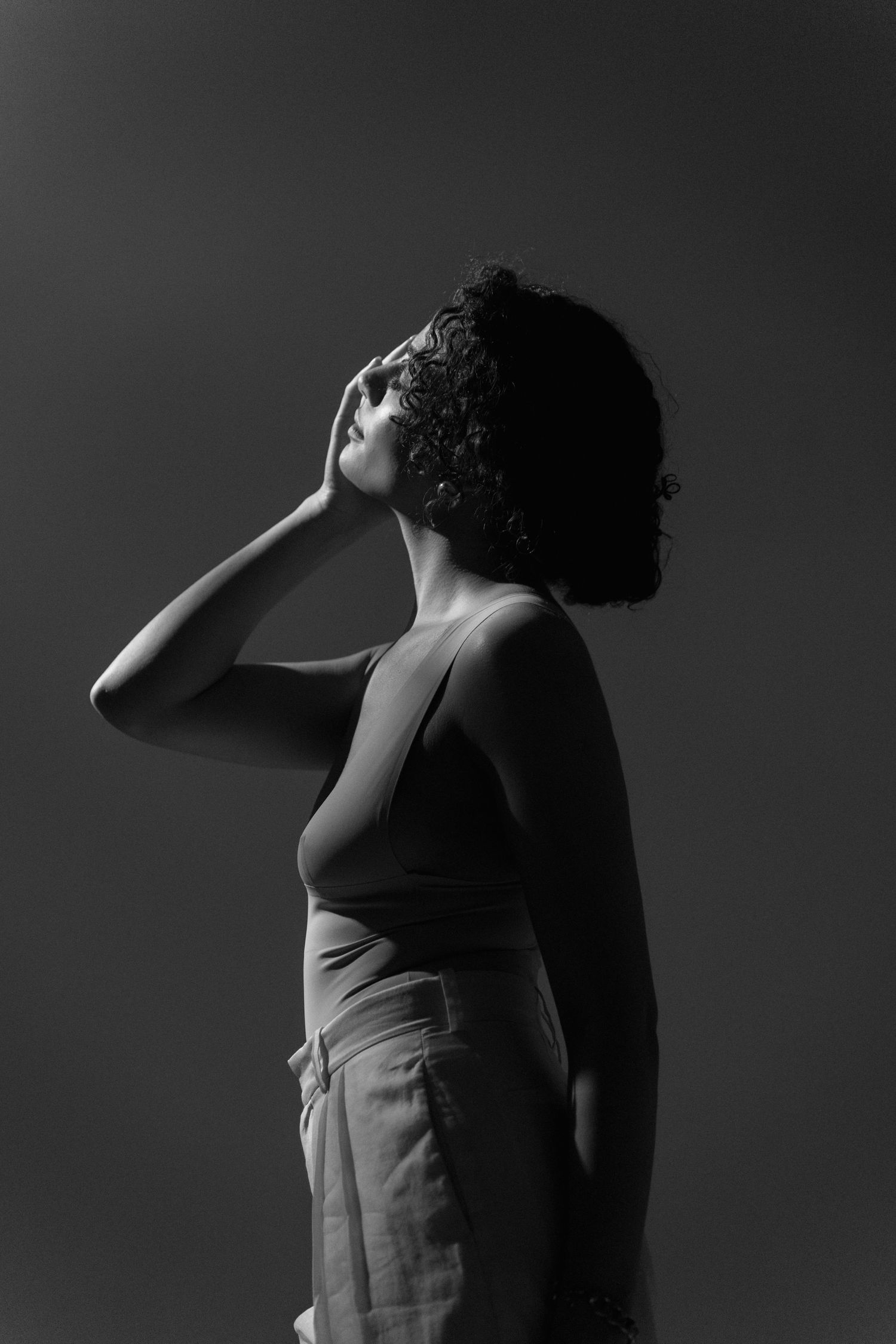 Black and white portrait of a woman with curly hair looking up with hand raised to her face.