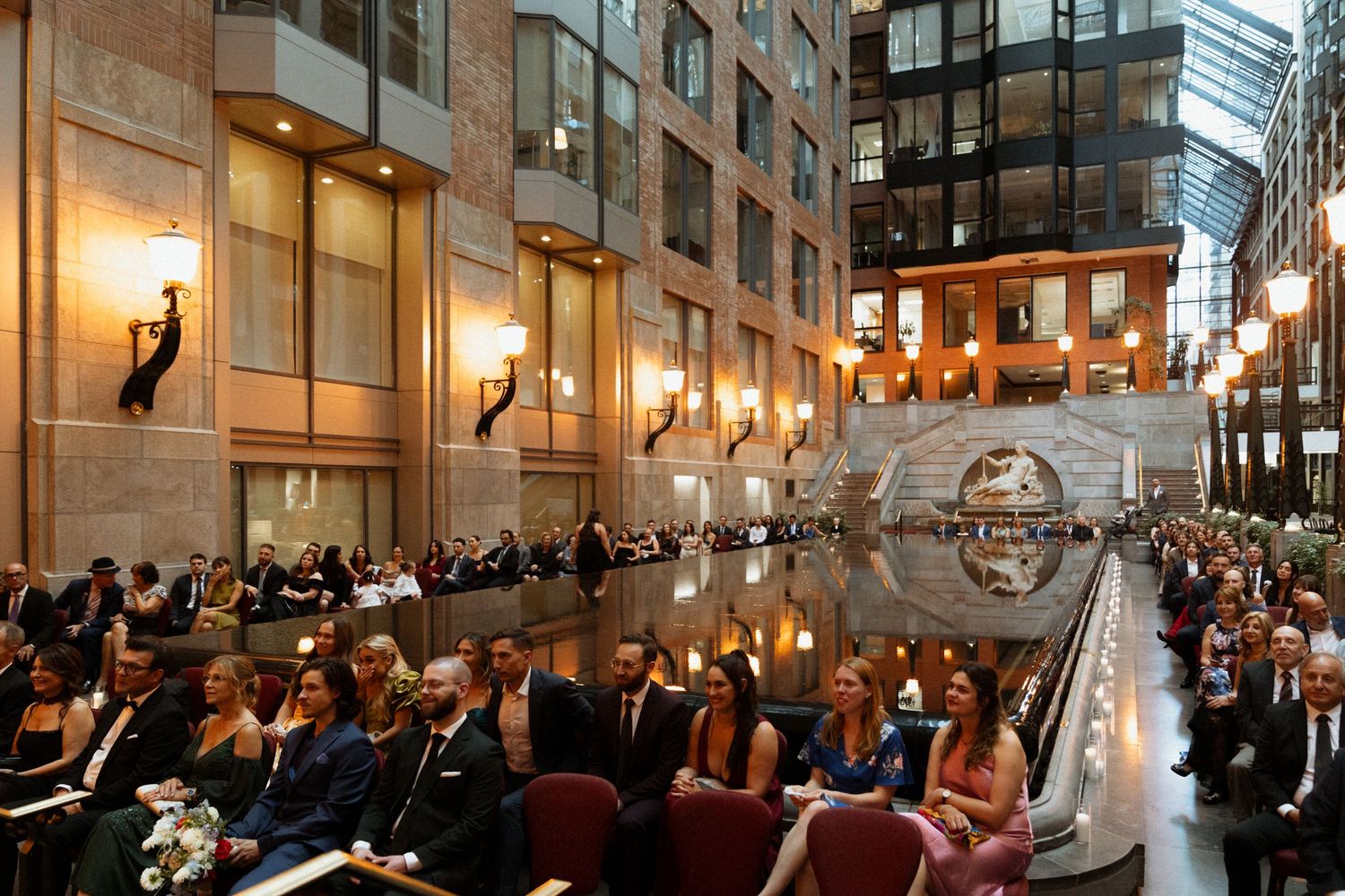 Wedding guests gather in an elegant ballroom with chandeliers and ornate decor for a formal ceremony.