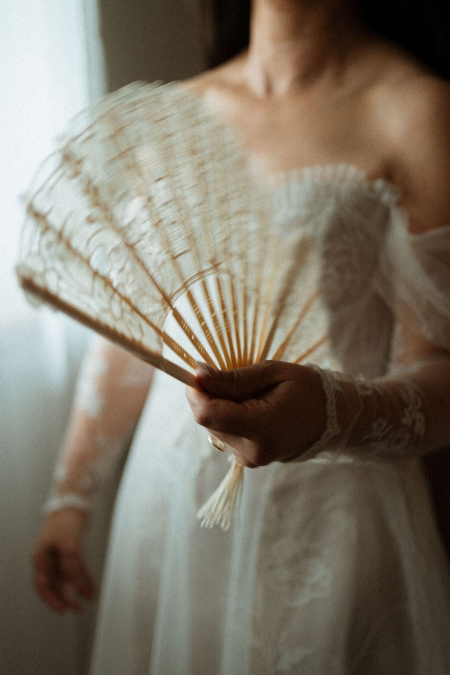 Delicate hand-held fan detail against a white wedding dress in soft focus.