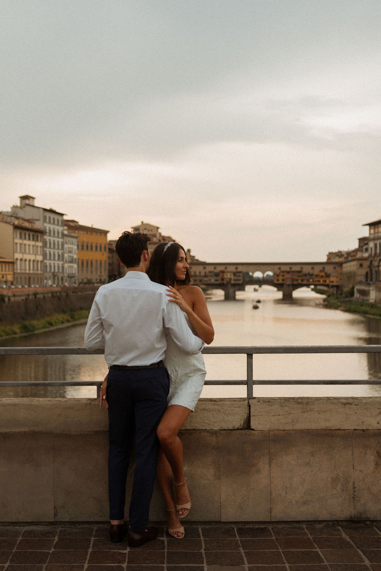 Couple enjoying sunset views over Arno River from bridge in Florence, Italy with historic architecture in background.