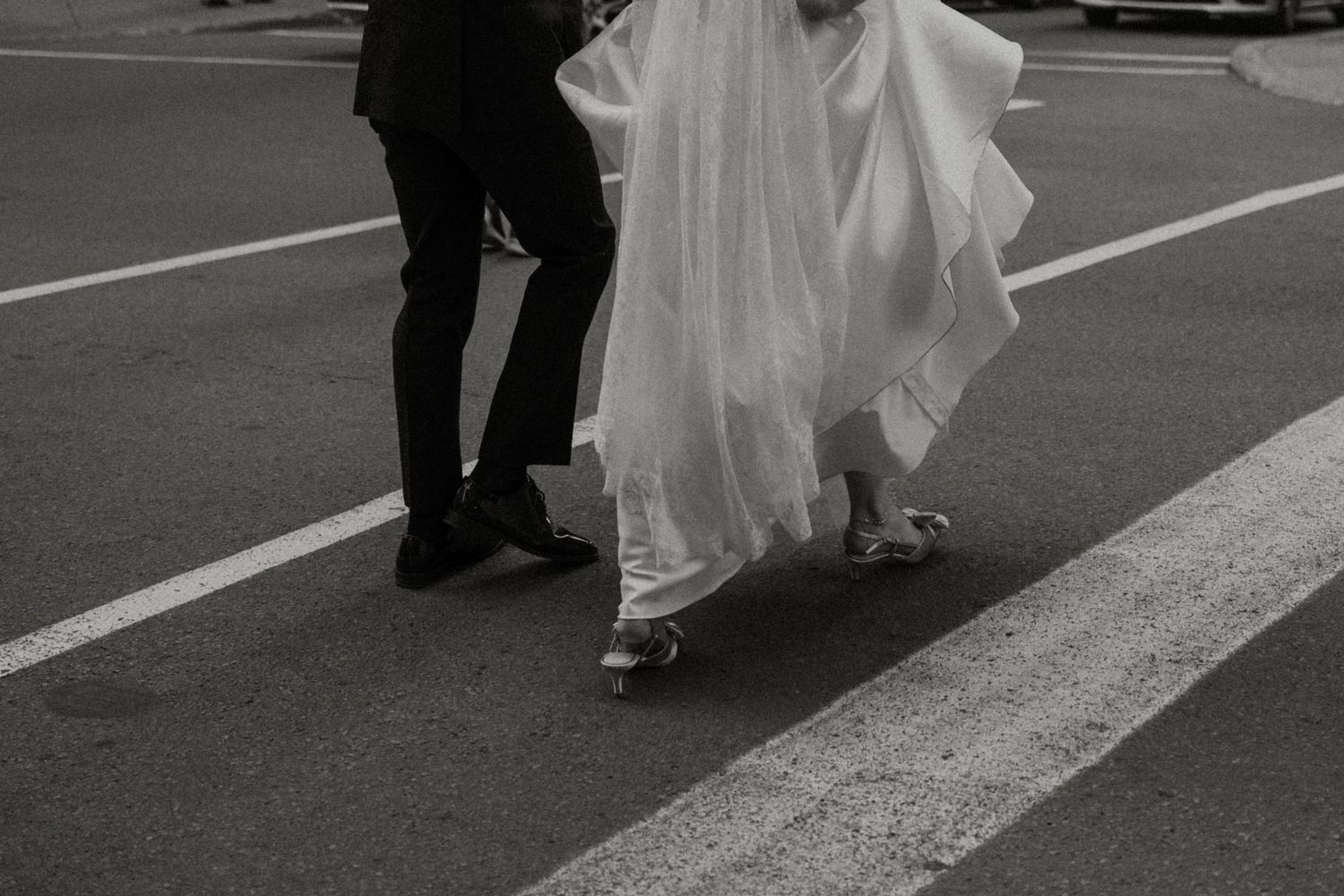 Black and white photo of a wedding dress trailing along a paved walkway.