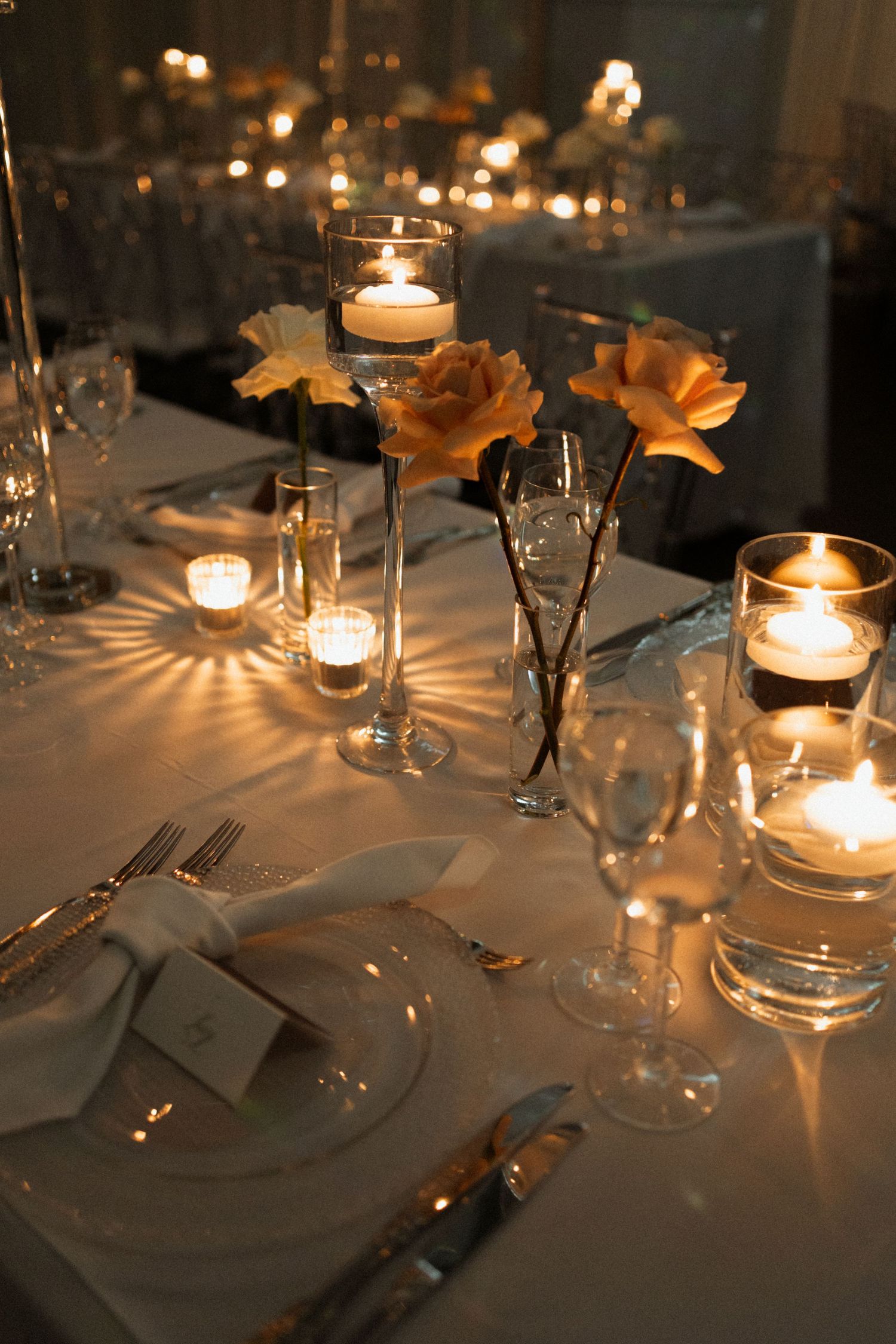 Elegant candlelit table setting with white linens, glassware and golden floral decorations creates romantic ambiance.