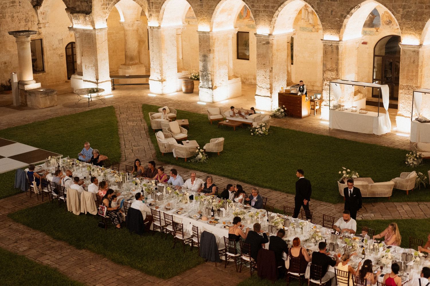Outdoor wedding reception under stone arches with elegant table settings and warm lighting.