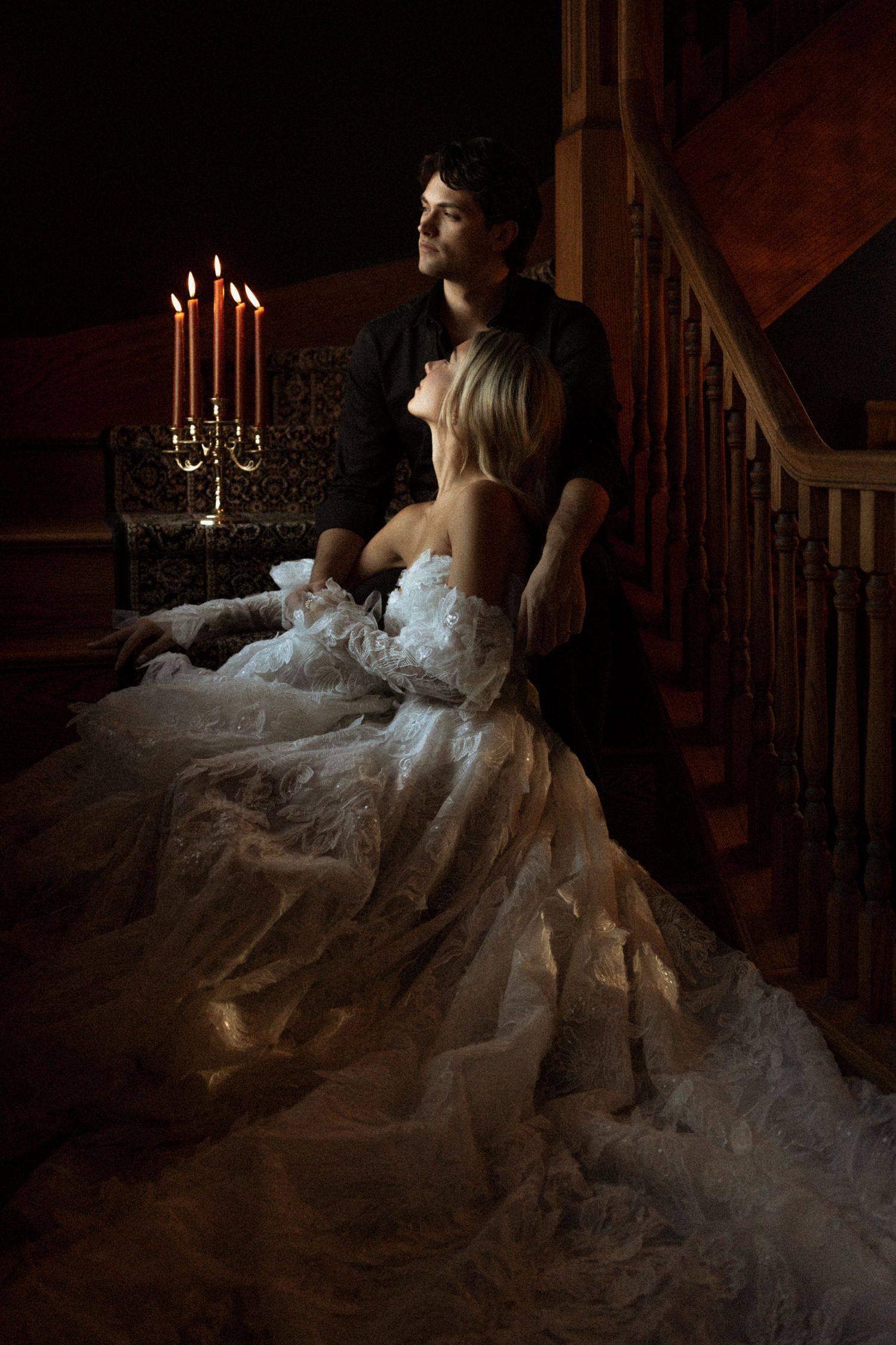 A romantic scene with a flowing white gown cascading down wooden stairs in dim candlelight.